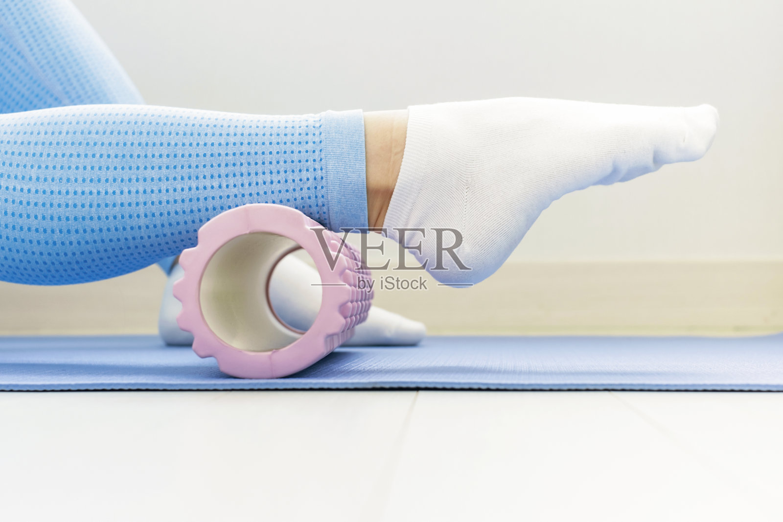 女性腿滚动按摩泡沫辊在蓝色背景，侧视图特写。照片摄影图片