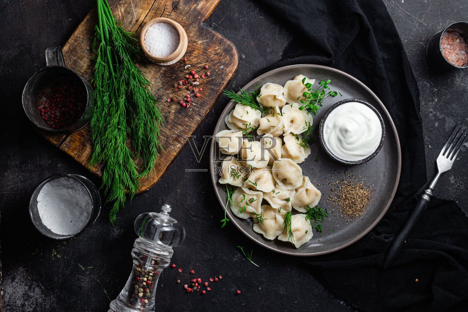 饺子加酸奶油和香草，放在一个深色的盘子里。肉饺子照片摄影图片