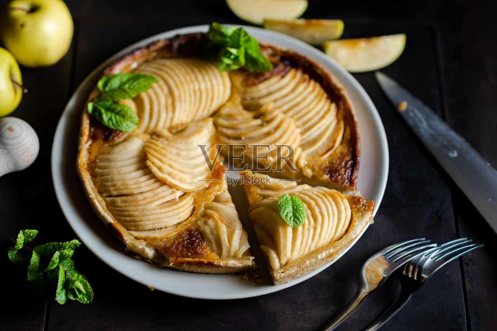 苹果法式派:黑色背景上的诱惑。传统的开放式派，有切成薄片的苹果，饰以薄荷叶。照片摄影图片