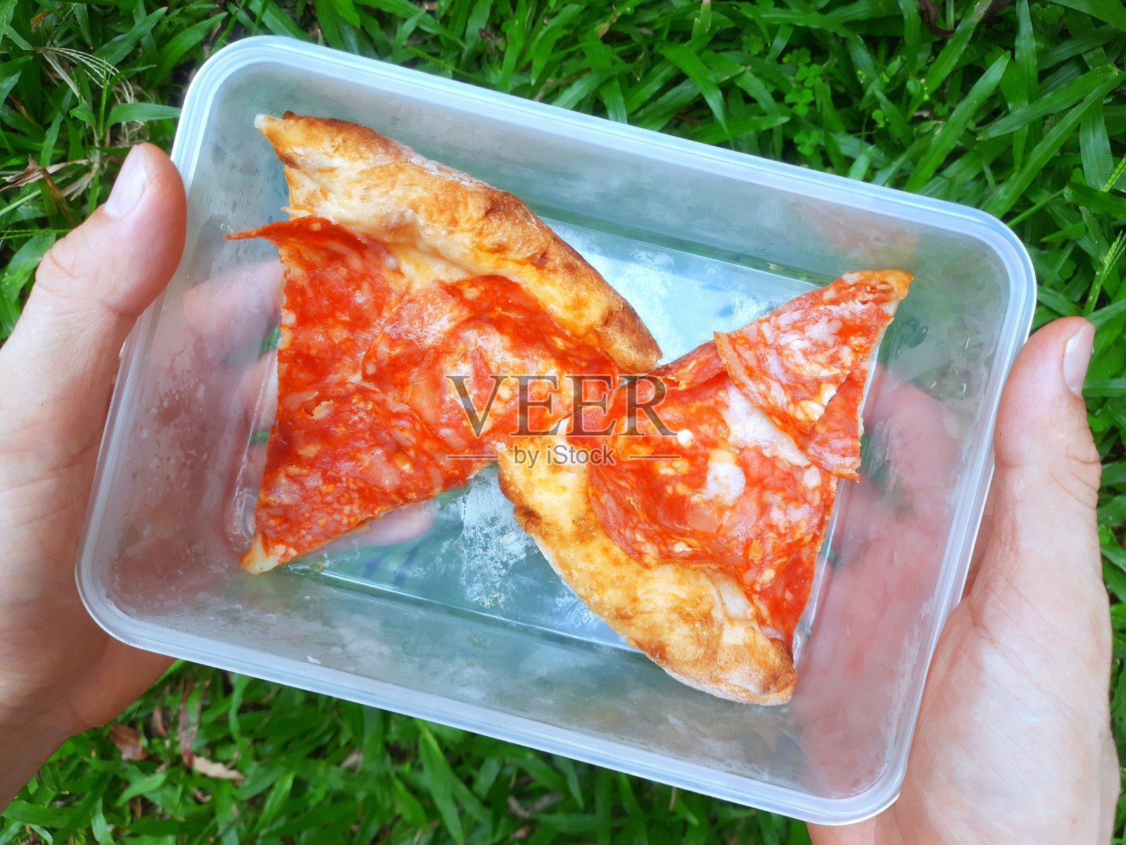 手拿塑料容器里的剩披萨。照片摄影图片