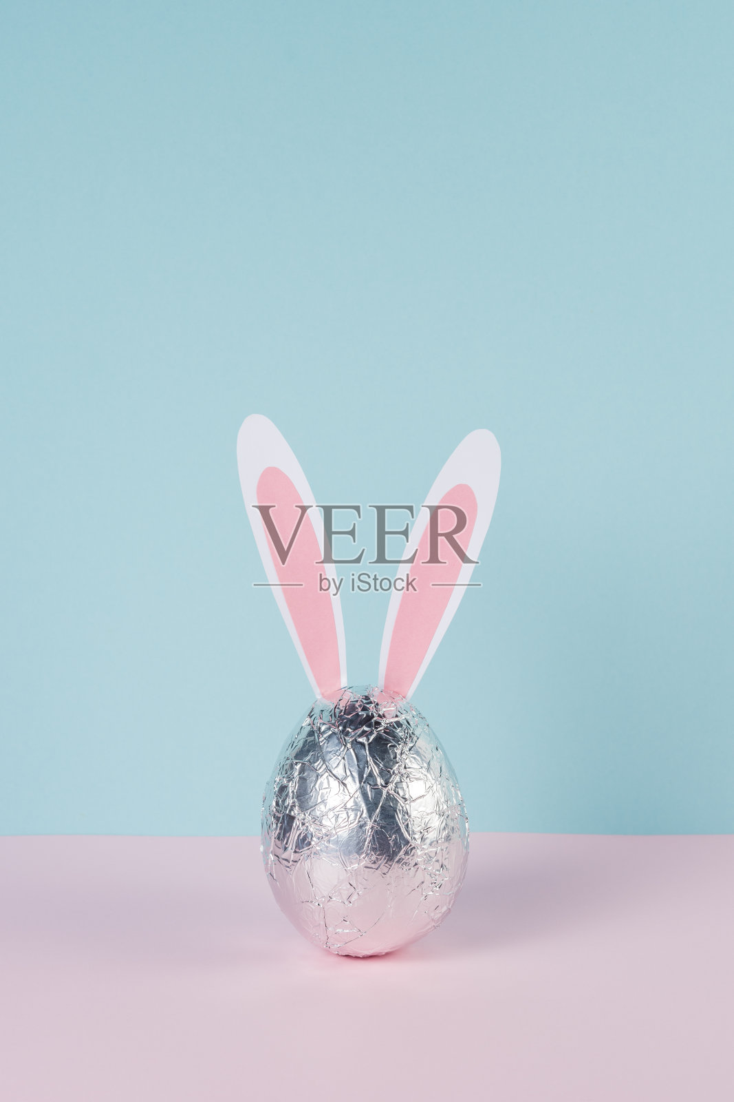 复活节彩蛋包在银箔与兔子或兔子耳朵。最小的粉彩粉和蓝色复活节假期的概念。照片摄影图片