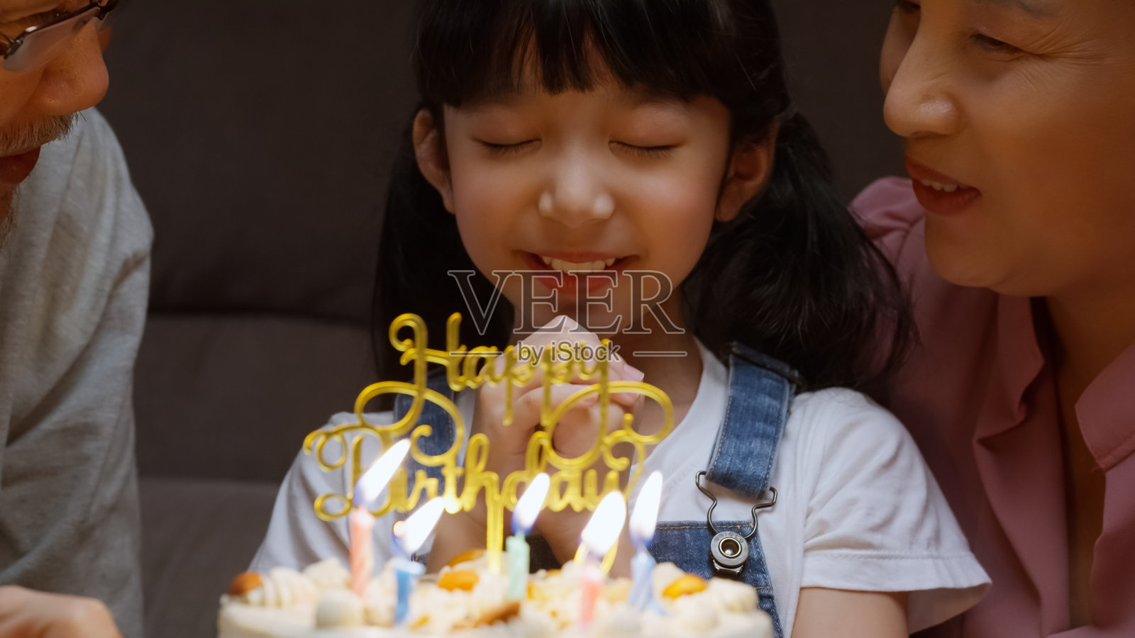 快乐的女孩在家人的簇拥下许愿，吹灭蛋糕上的蜡烛照片摄影图片