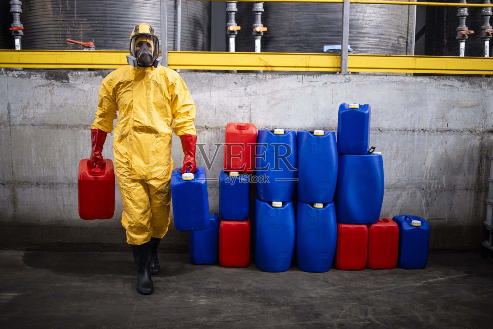 穿着防护服和防毒面具的化工工人在工厂搬运危险物品。照片摄影图片