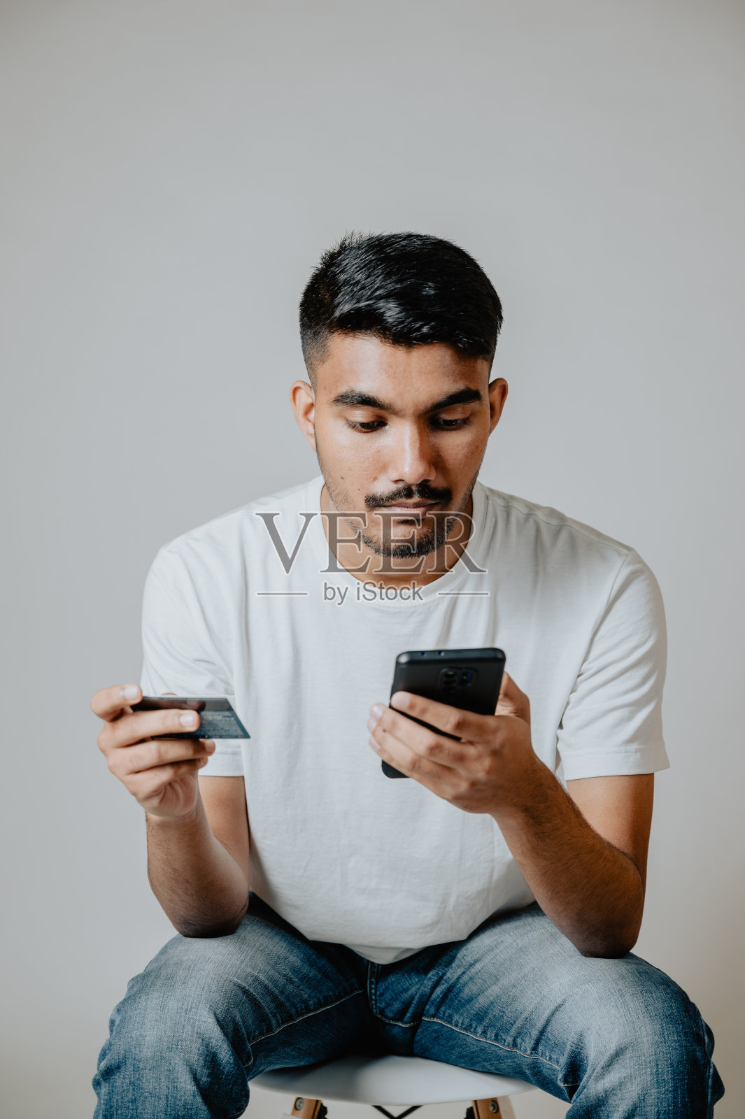 年轻的印度男性在工作室使用手机和信用卡照片摄影图片