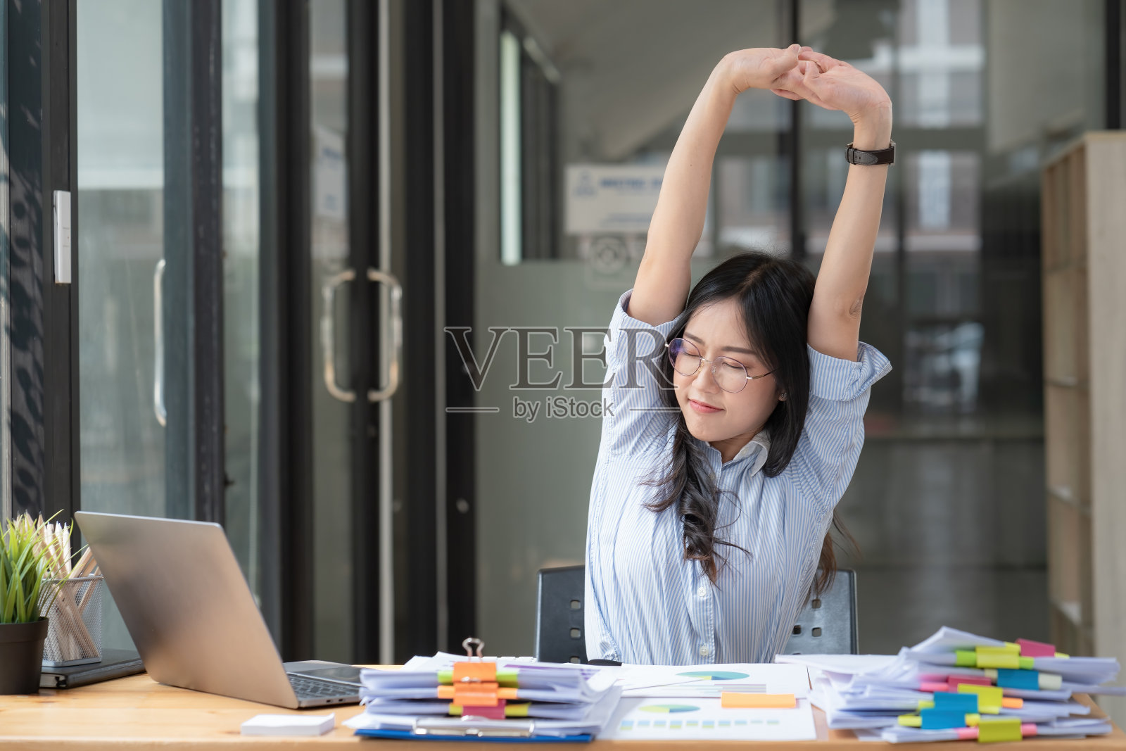 亚洲女商人在工作劳累时，会做伸展手臂的姿势来放松身体。疲惫的亚洲妇女在办公室工作时伸展双手。照片摄影图片