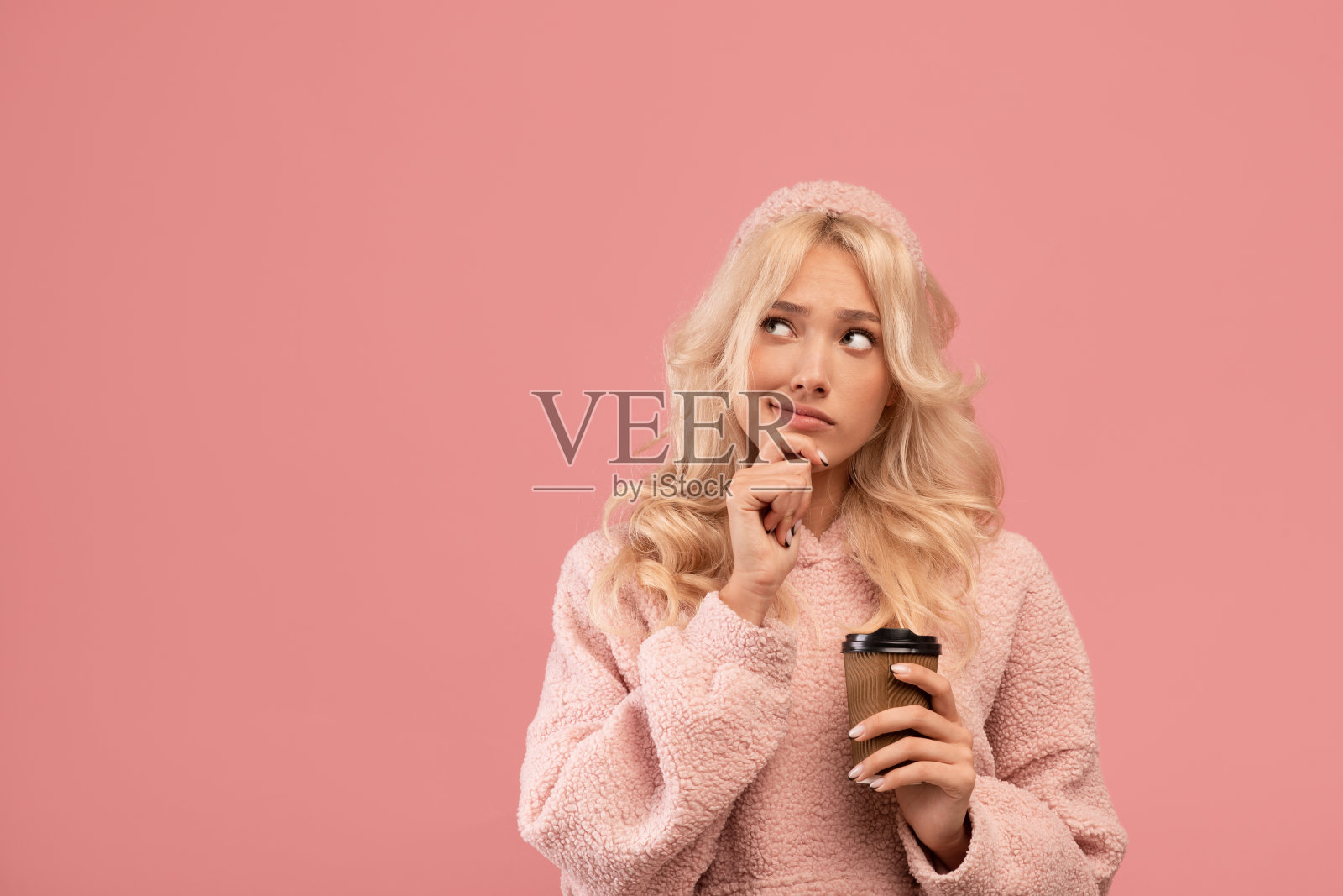 沉思的女人拿着外卖咖啡，琢磨着提供的东西，看着一旁的空地，抚摸着下巴照片摄影图片