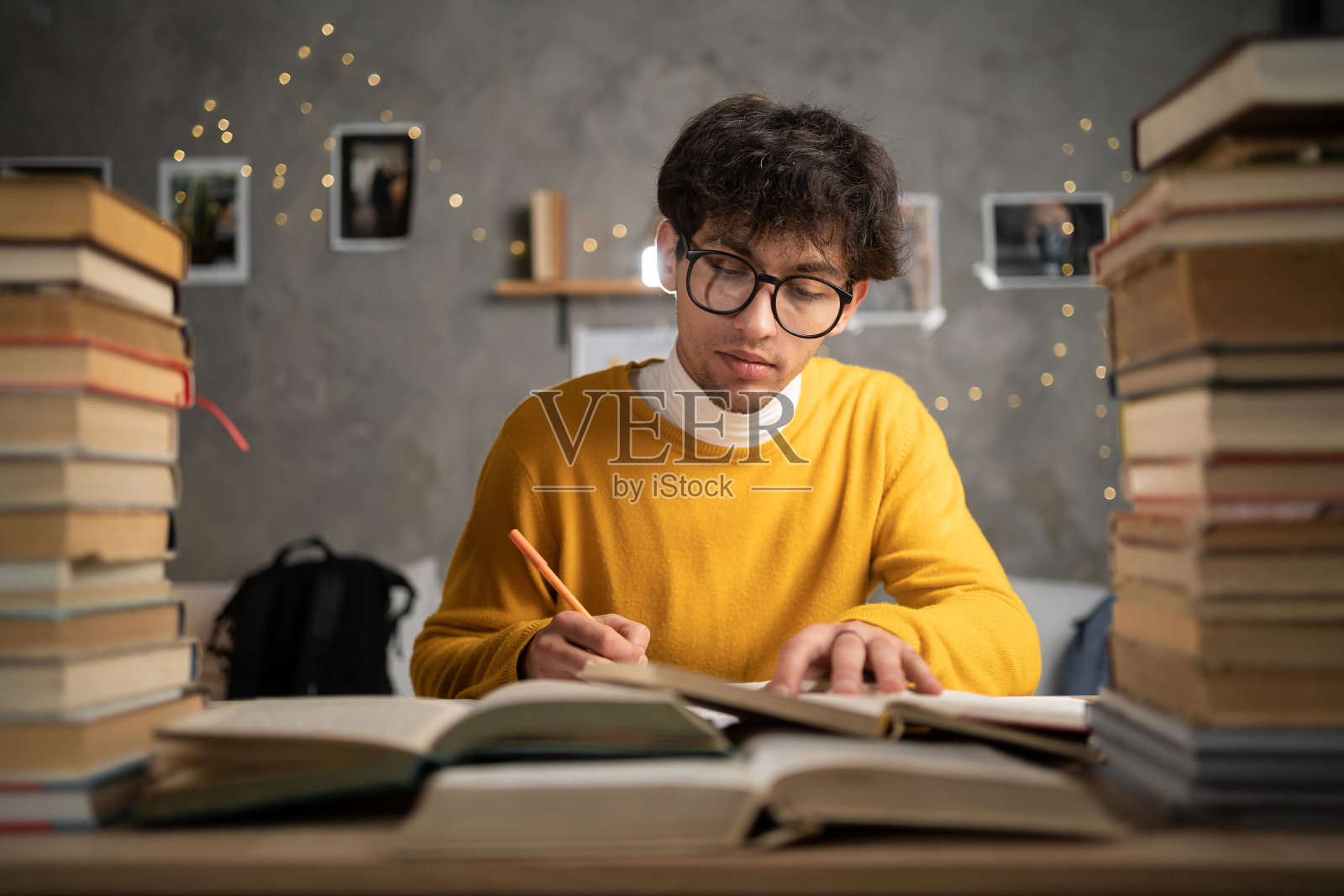 教育的概念。阿拉伯学生在宿舍的桌子上学习，桌上有成堆的书，年轻的男子准备考试，晚上在笔记本上做笔记。照片摄影图片