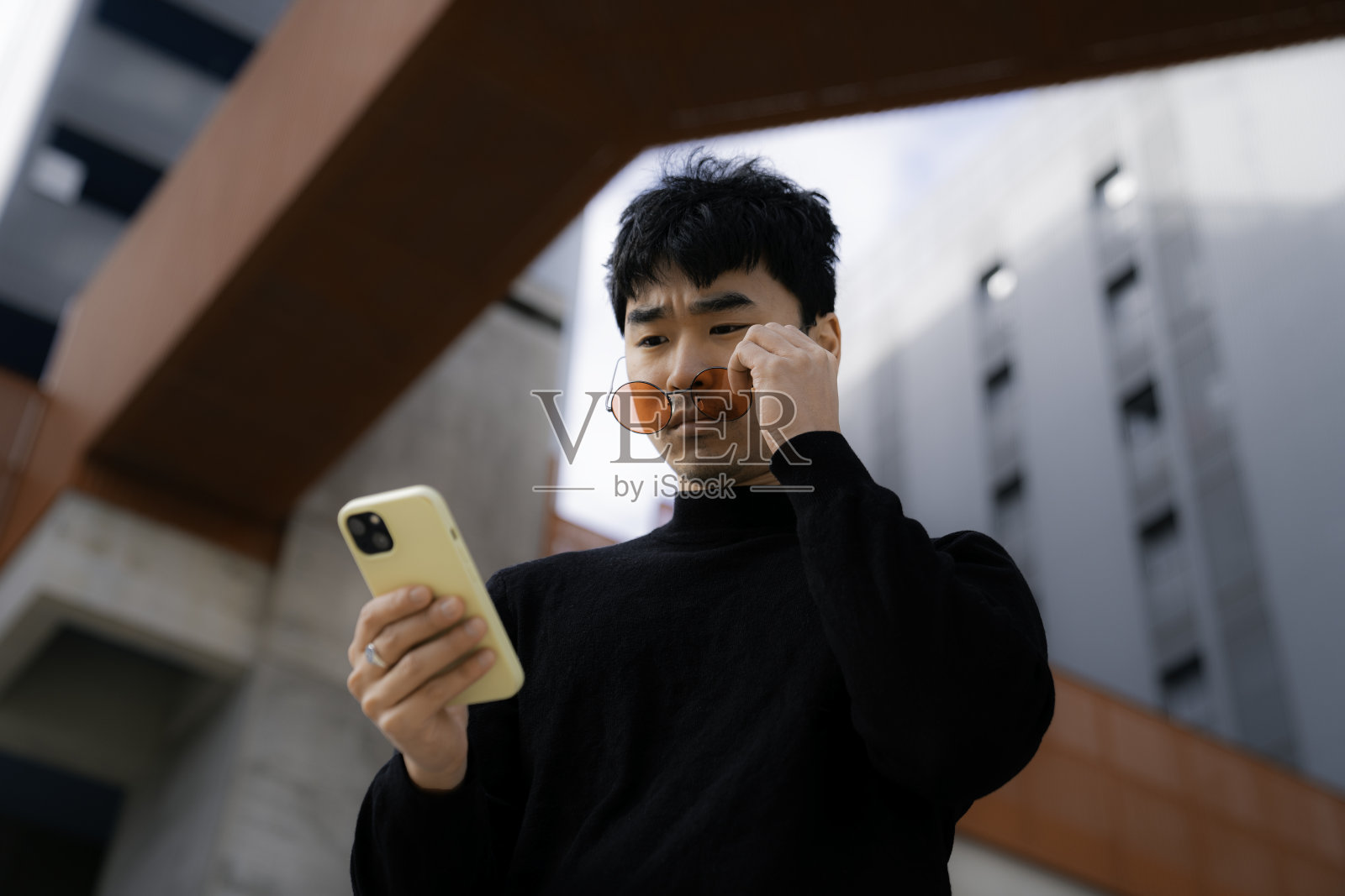 年轻的亚洲男子带着凉爽的红色眼镜，惊讶地看着手机照片摄影图片