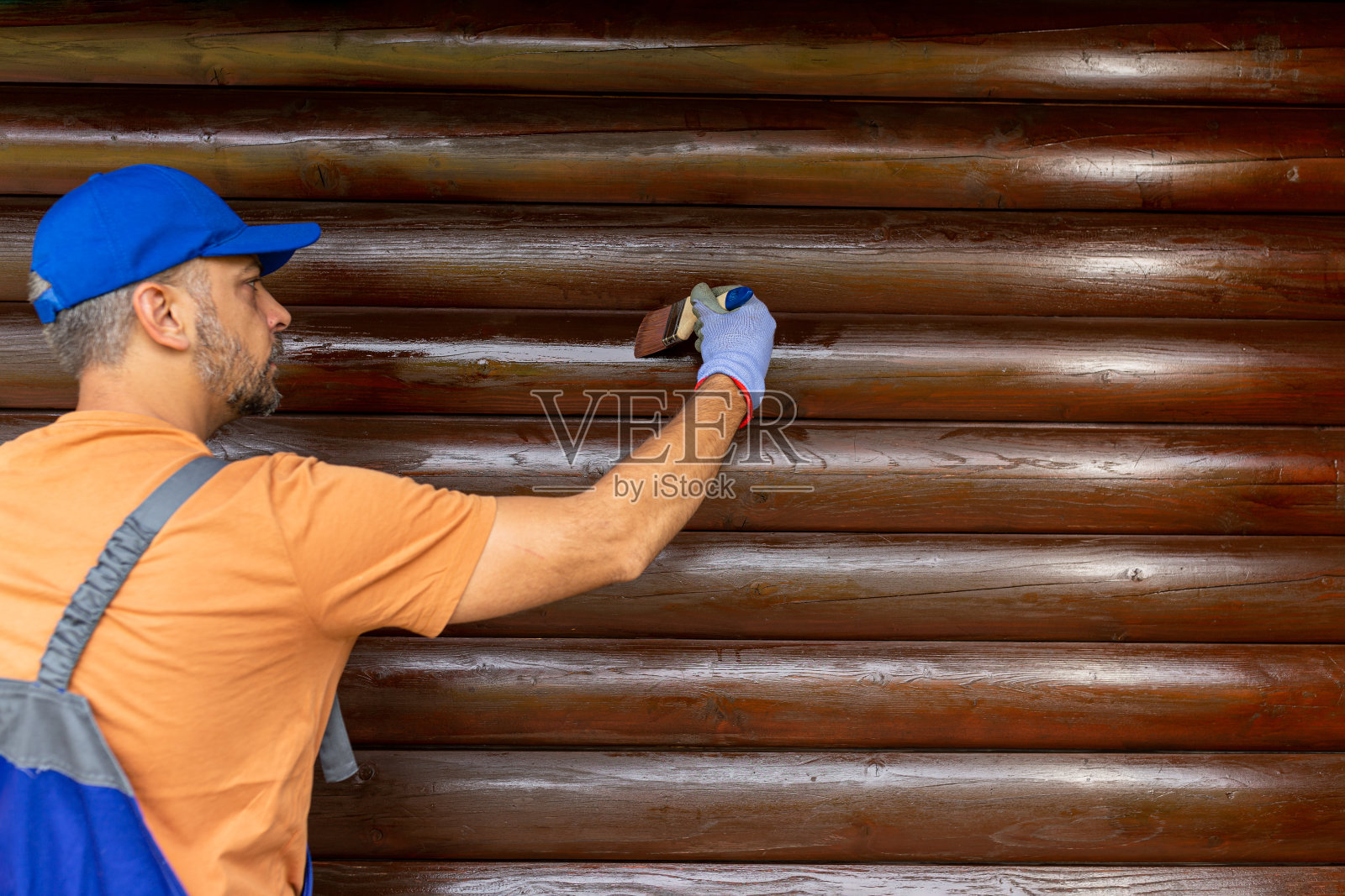 工人用刷子在木屋外墙上涂抹污渍。照片摄影图片