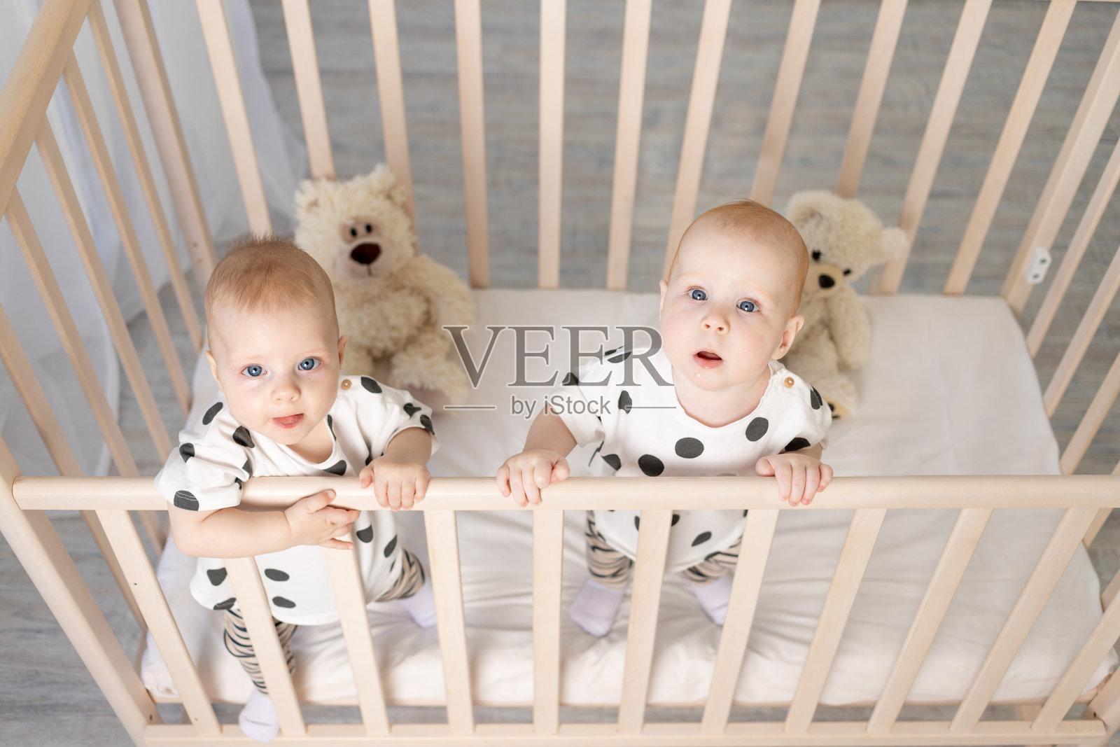 两个8个月大的双胞胎弟弟和妹妹穿着睡衣坐在婴儿床上，看着摄像头，俯视图，友谊的概念，一个发短信的地方照片摄影图片