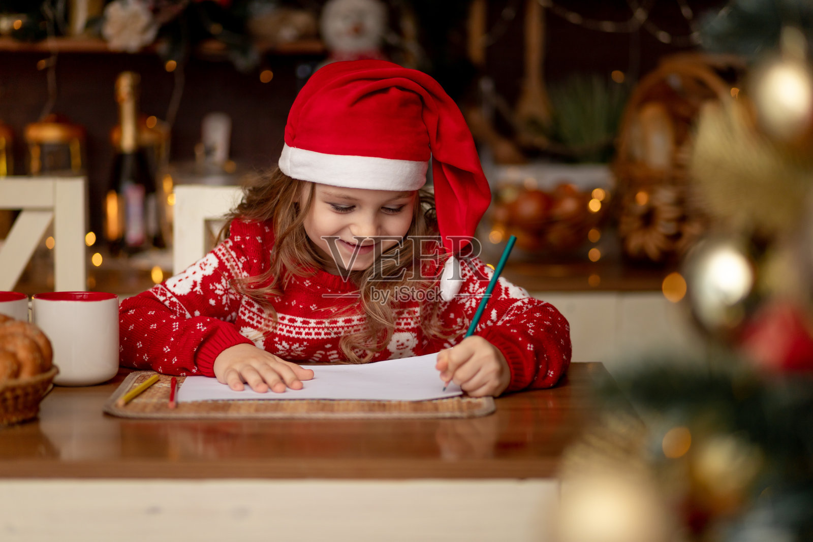 一个穿着红色毛衣，戴着帽子的可爱的小女孩，在一个有圣诞树的黑暗厨房里给圣诞老人写了一封信，等待着新的一年或圣诞节的到来照片摄影图片