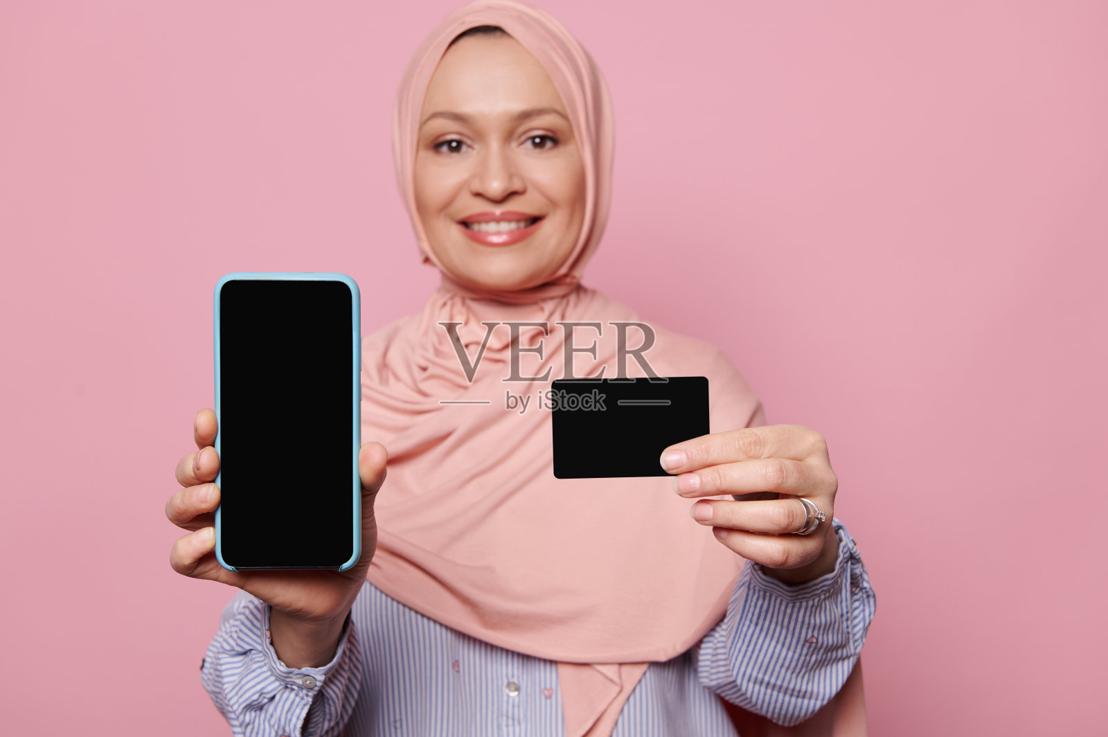 智能手机的黑屏和塑料信用卡，在一个模糊的微笑阿拉伯穆斯林妇女手中照片摄影图片