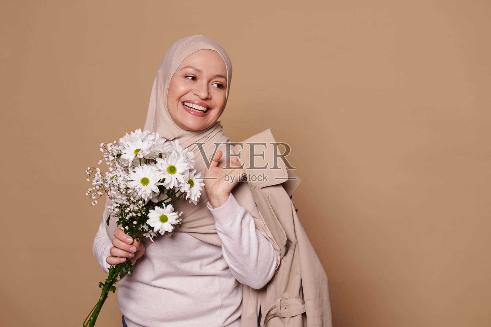 微笑的穆斯林孕妇戴着米色头巾，手捧洋甘菊照片摄影图片
