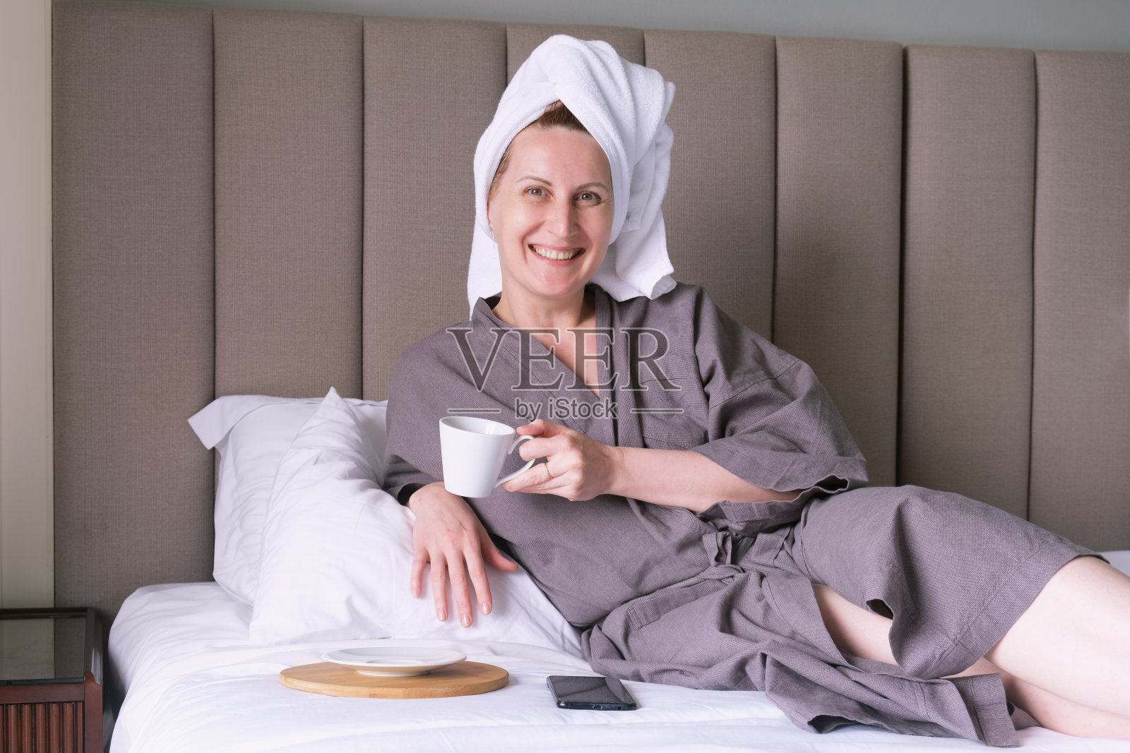 一个头上裹着毛巾的中年妇女在床上喝咖啡照片摄影图片