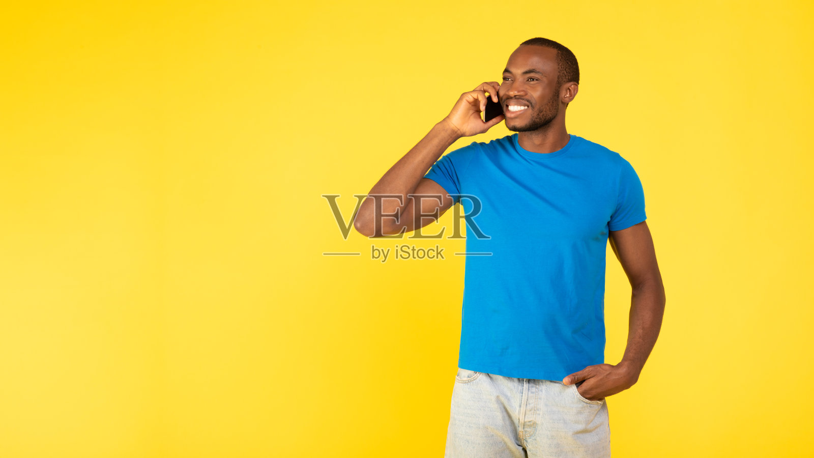 一个非洲裔美国人在打电话，看向一边，黄色背景照片摄影图片