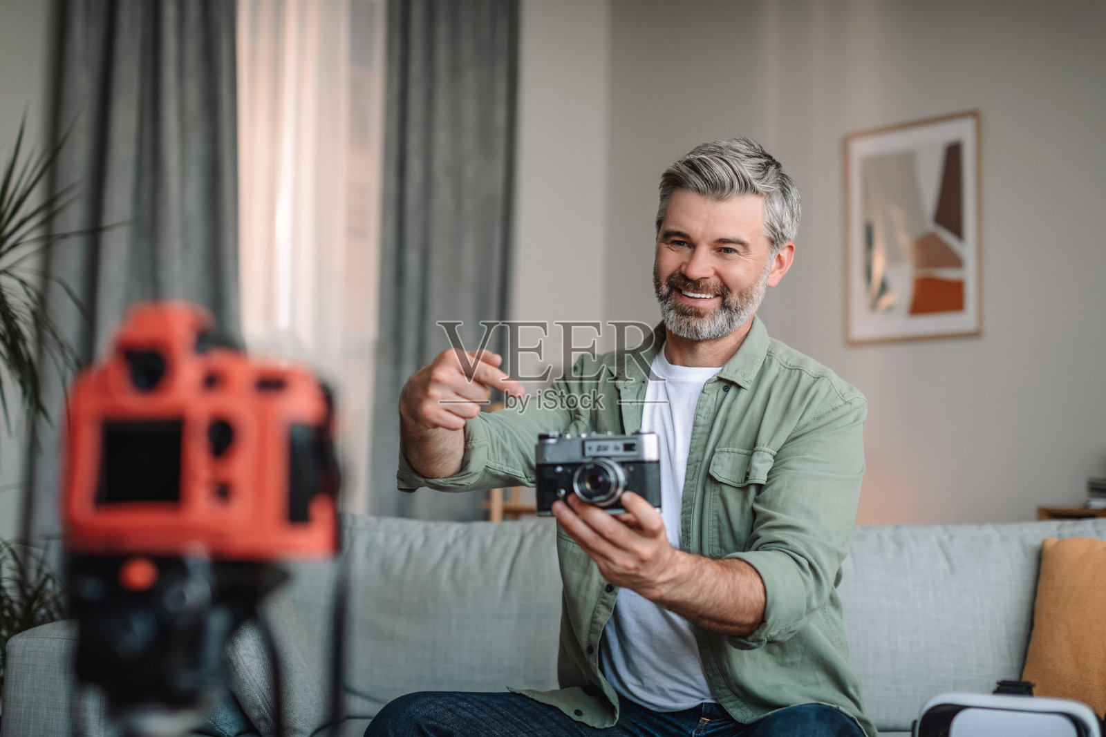 在家写博客。快乐的白种人大胡子男子展示照片相机和拍摄视频在房间里照片摄影图片