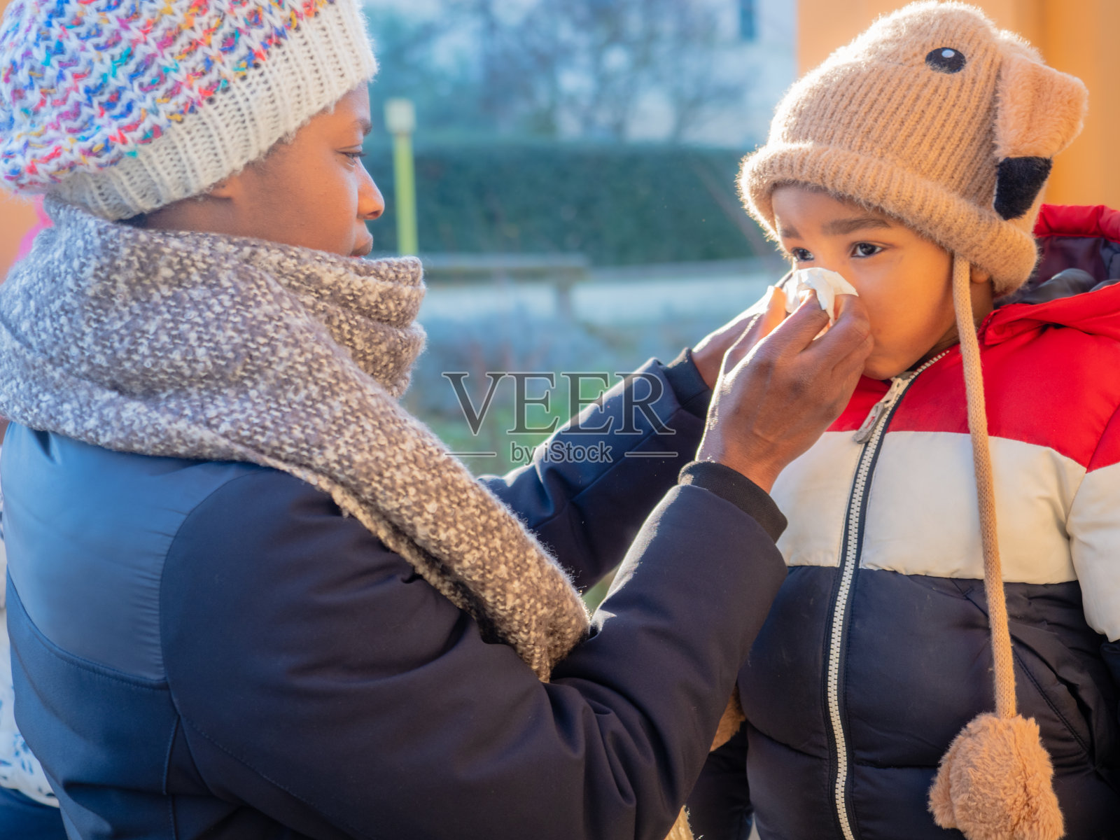 奶奶拥抱关心微笑的非洲裔美国孩子穿着温暖的羊毛无檐针织帽与耳盖在秋天冬天户外日落照片摄影图片