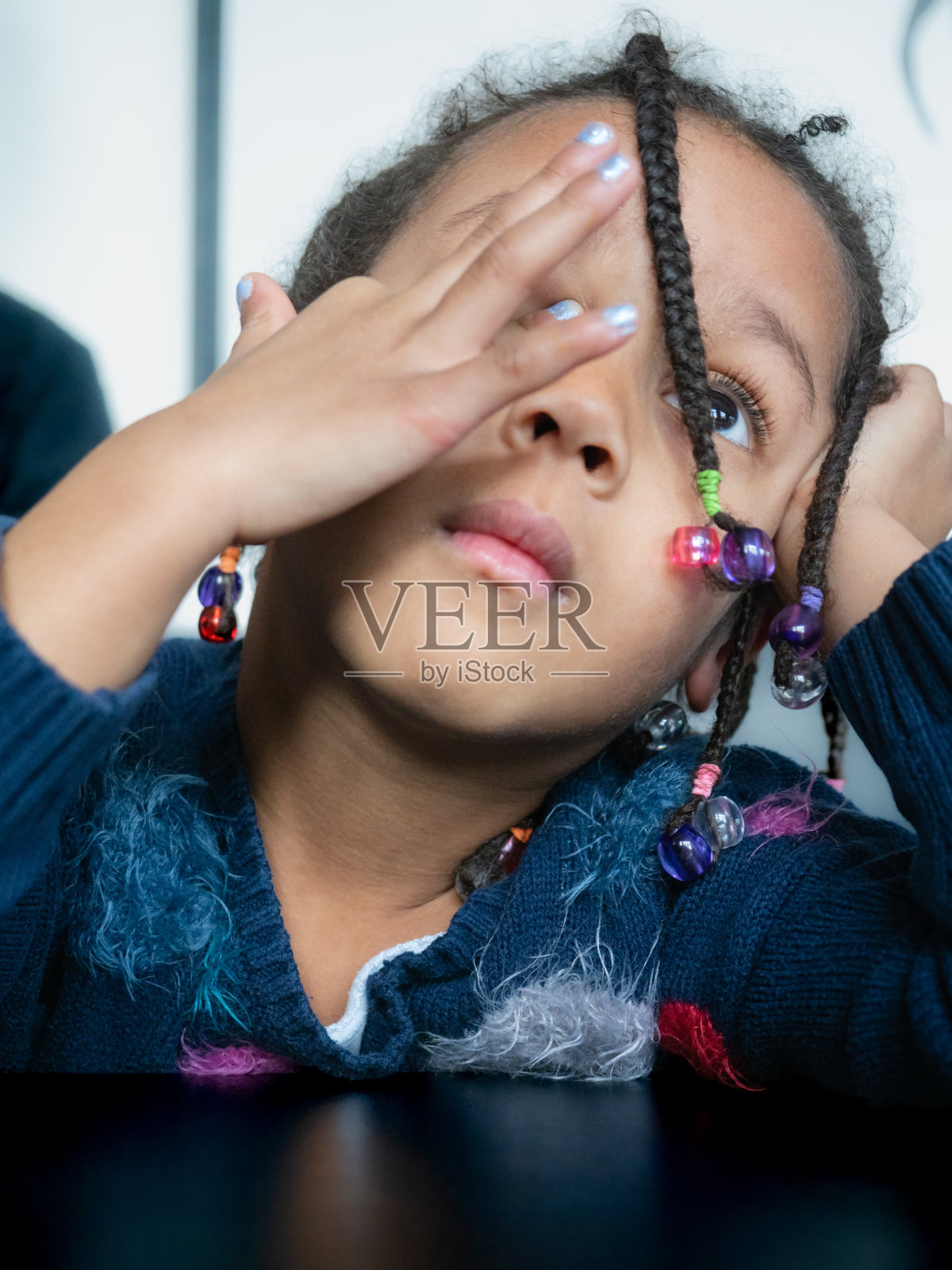 可爱的小非裔美国女孩与辫子发型累和无聊的桌子在室内照片摄影图片