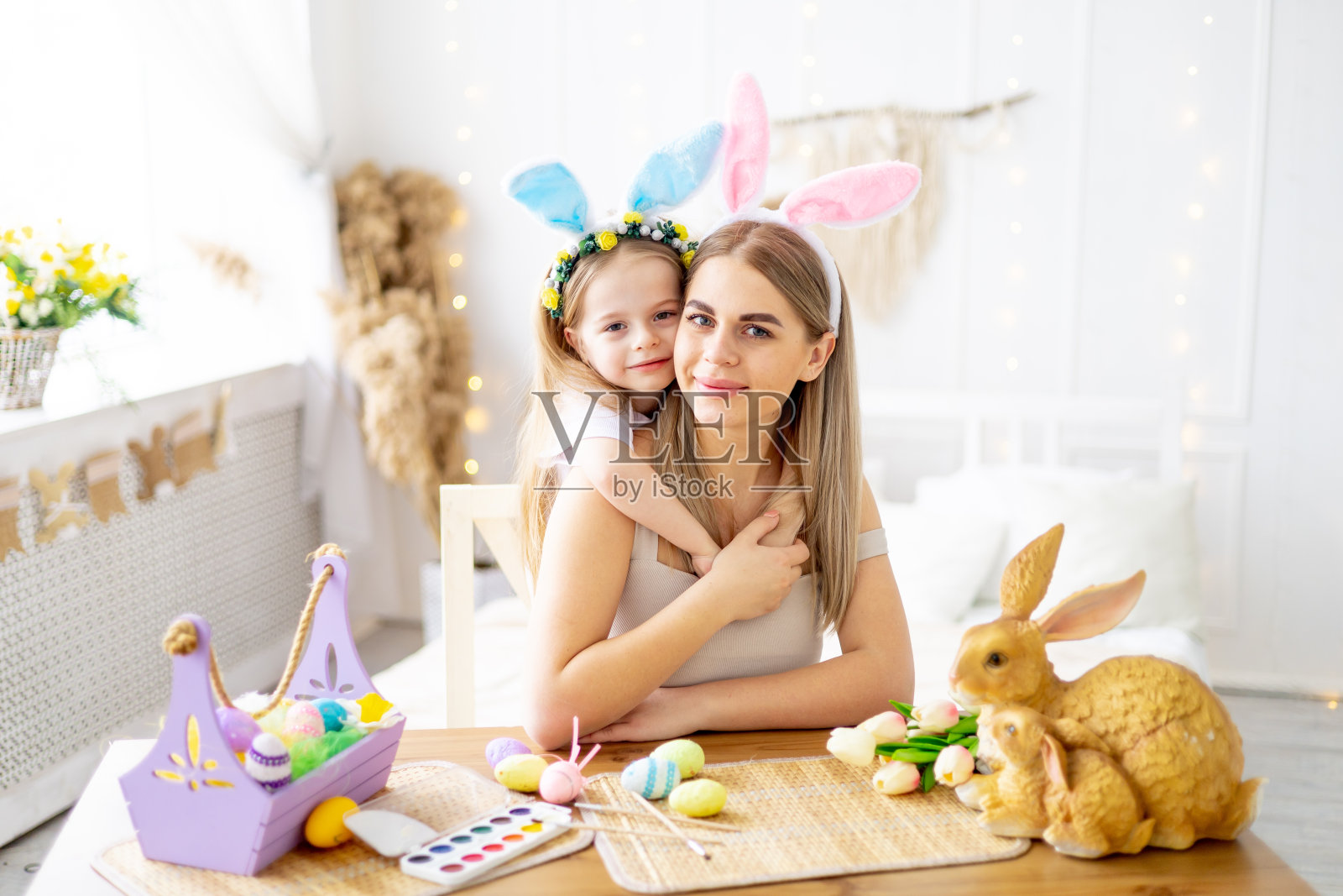 复活节，一位母亲带着头上戴着野兔耳朵的小女儿正在为这个节日做准备，他们温柔地拥抱和亲吻，一起度过时光，五彩缤纷的鸡蛋，生活方式，照片摄影图片