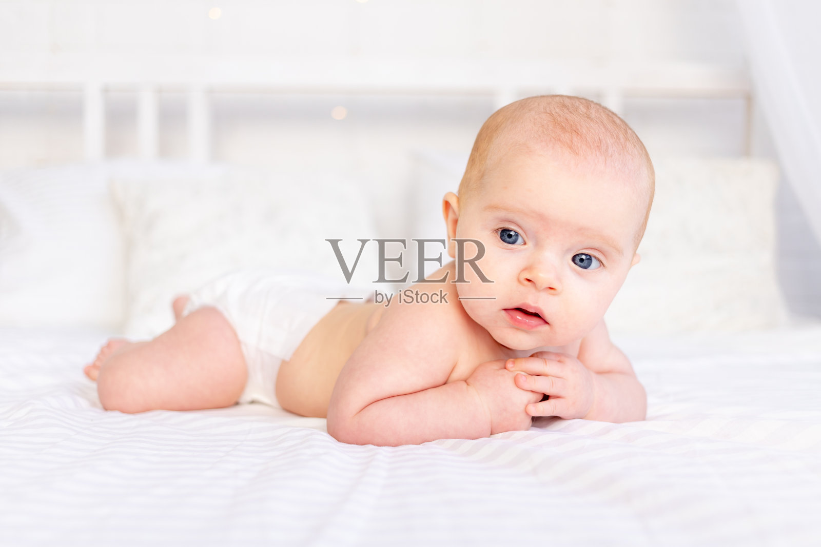 可爱的女婴在婴儿床上趴在白色棉床上，在婴儿室里微笑着，新生的早晨照片摄影图片