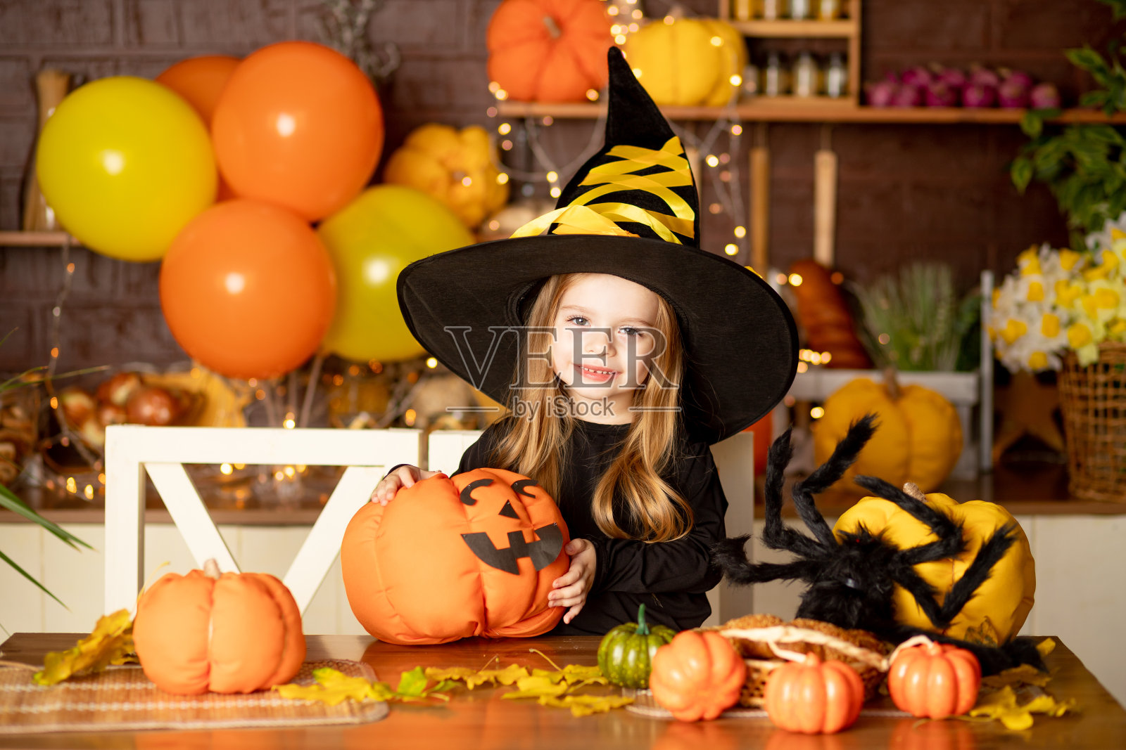 万圣节前夕，一个穿着女巫服装的小女孩在黑暗的厨房里用南瓜和一只大蜘蛛装饰南瓜照片摄影图片