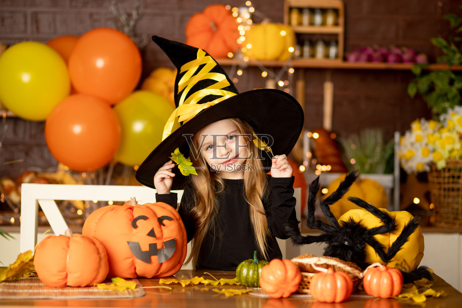 在万圣节前夕，一个女孩穿着女巫服装，拿着南瓜和一只大蜘蛛，在黑暗的厨房里害怕或玩树叶照片摄影图片