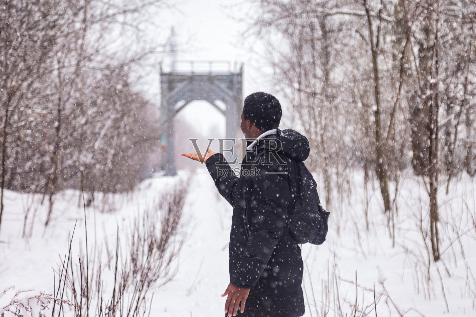 后视图非洲裔美国人站在铁路轨道上，在大雪纷飞的冬天在农村森林外，飘落的雪。黑人在外面抓雪花。休闲活动概念。复制文本空格照片摄影图片