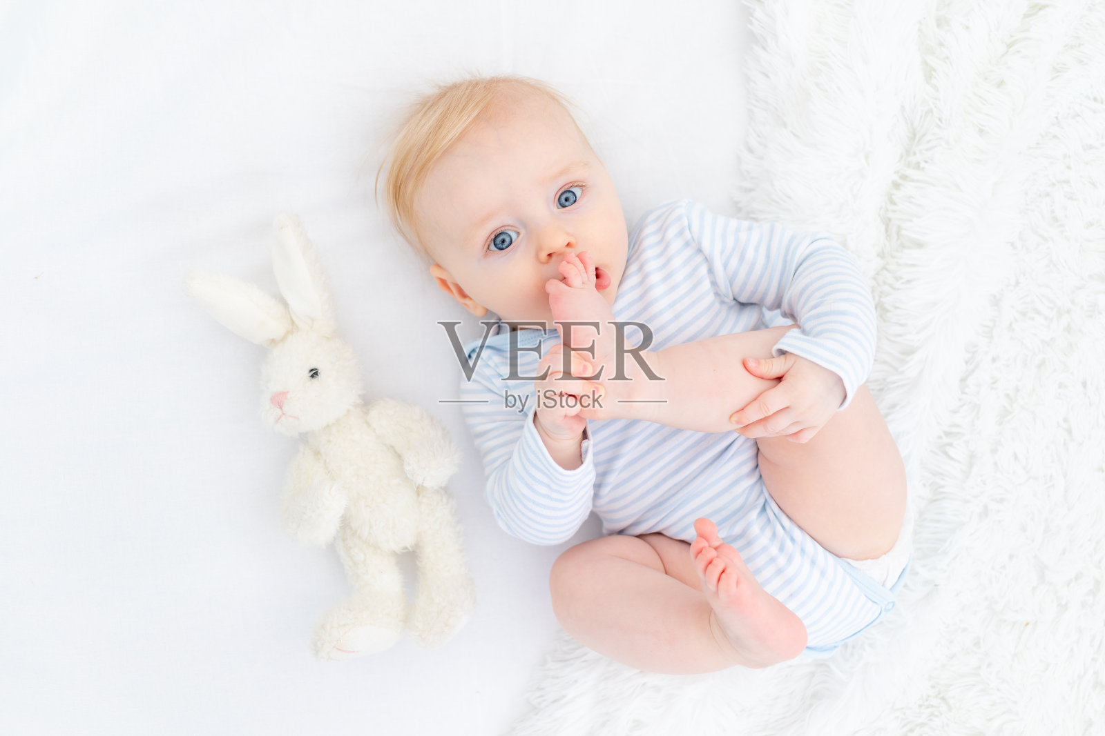 婴儿吮脚躺在床上，男婴金发六个月照片摄影图片