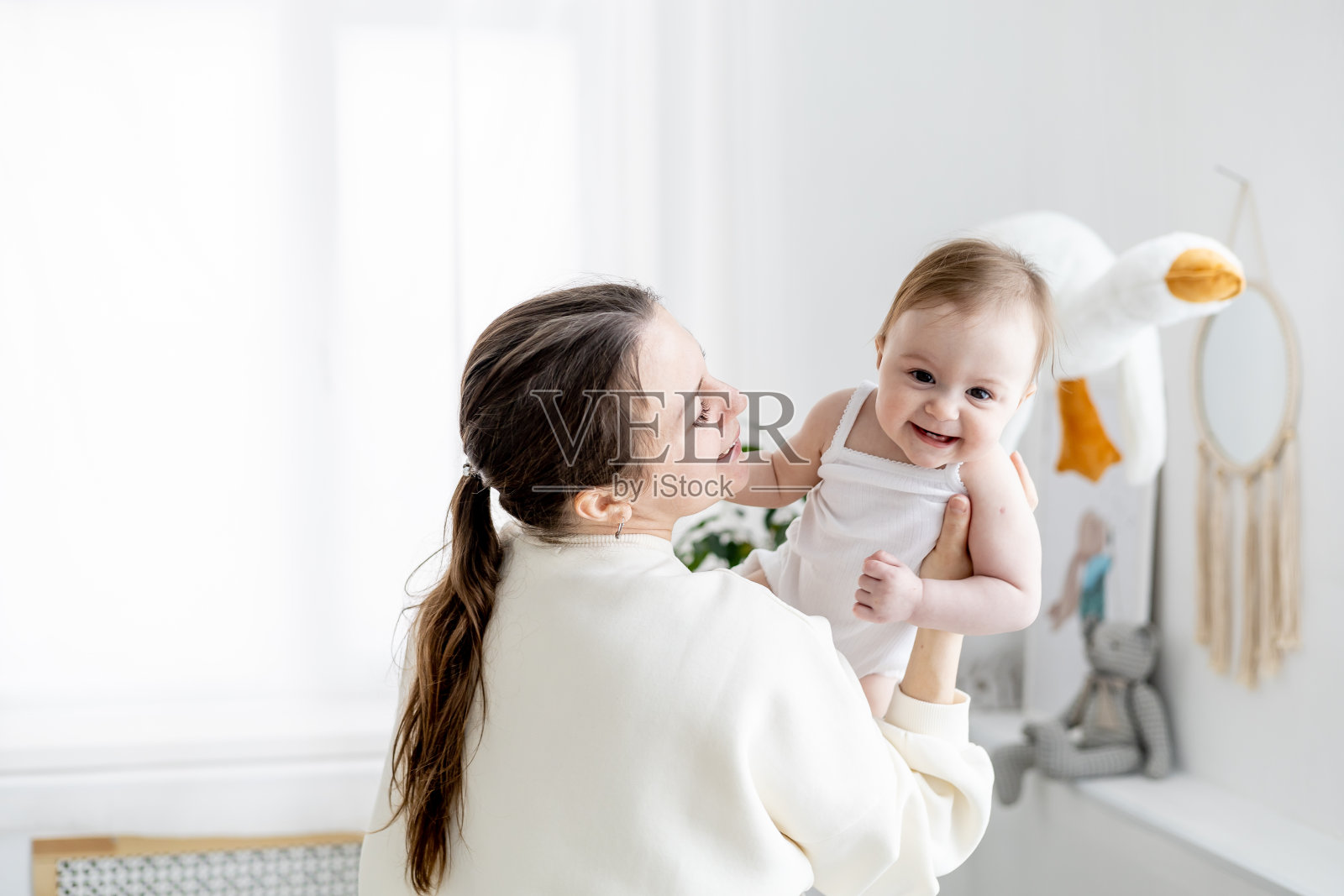 在孩子们明亮的房间里，妈妈温柔地亲吻和拥抱她的小女儿，一起享受家庭、母亲和对婴儿的爱照片摄影图片