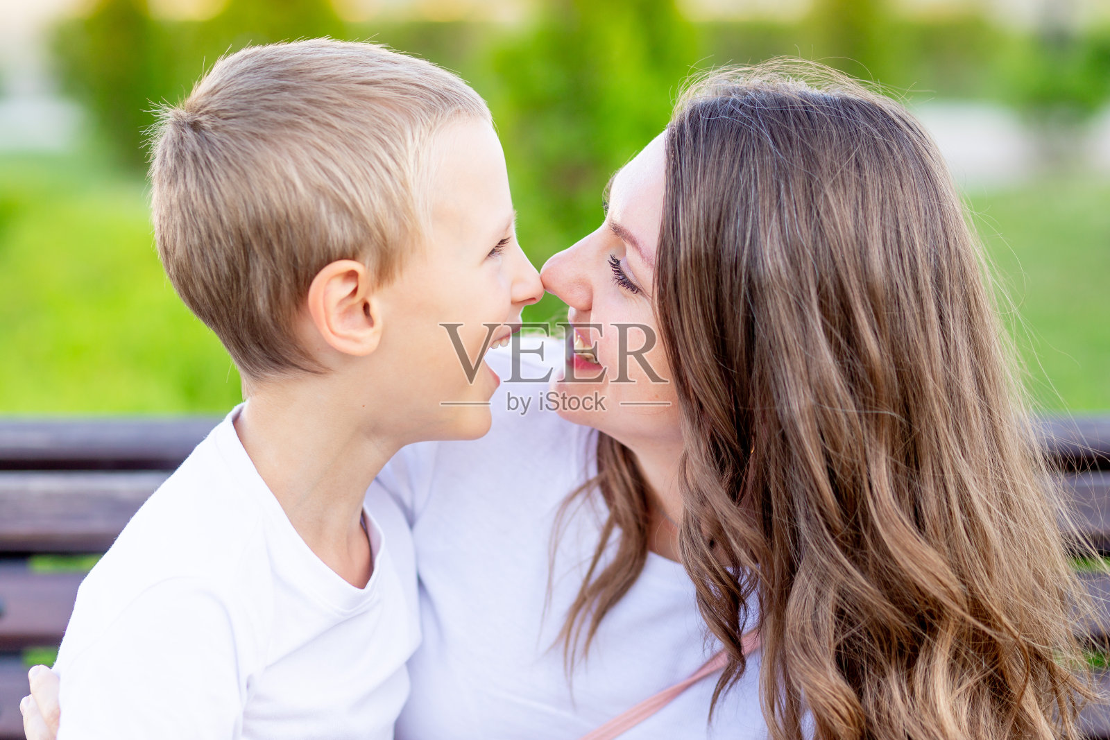 一个母亲和她的儿子在公园的长椅上的大肖像在夏天有乐趣拥抱，笑和玩照片摄影图片