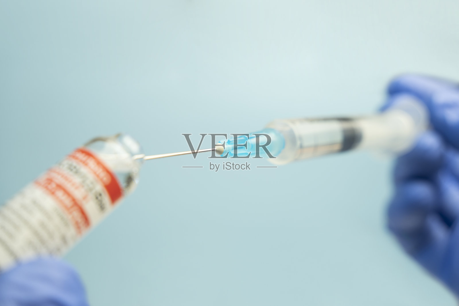 蓝色背景上，医生手中的注射器与疫苗特写照片摄影图片