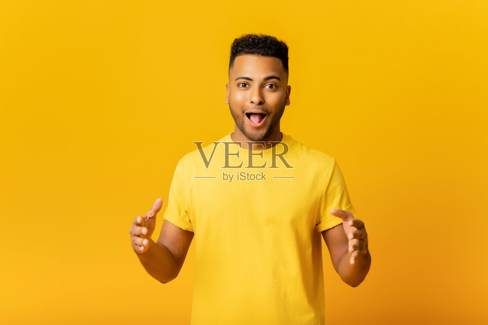 兴奋惊讶的印度人手牵着手在他面前，展示一些东西，震惊的阿拉伯人拿着你的产品隔离在黄色的空间，展示大小照片摄影图片