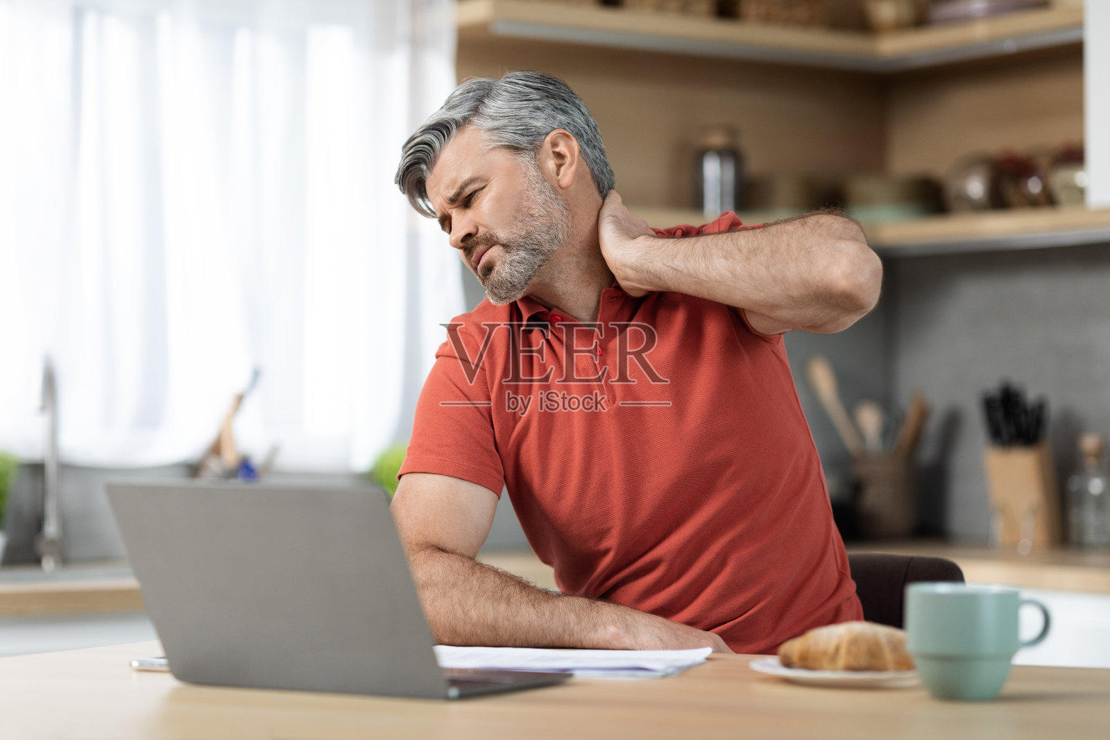 疲惫的男人坐在笔记本电脑前，摸着脖子照片摄影图片