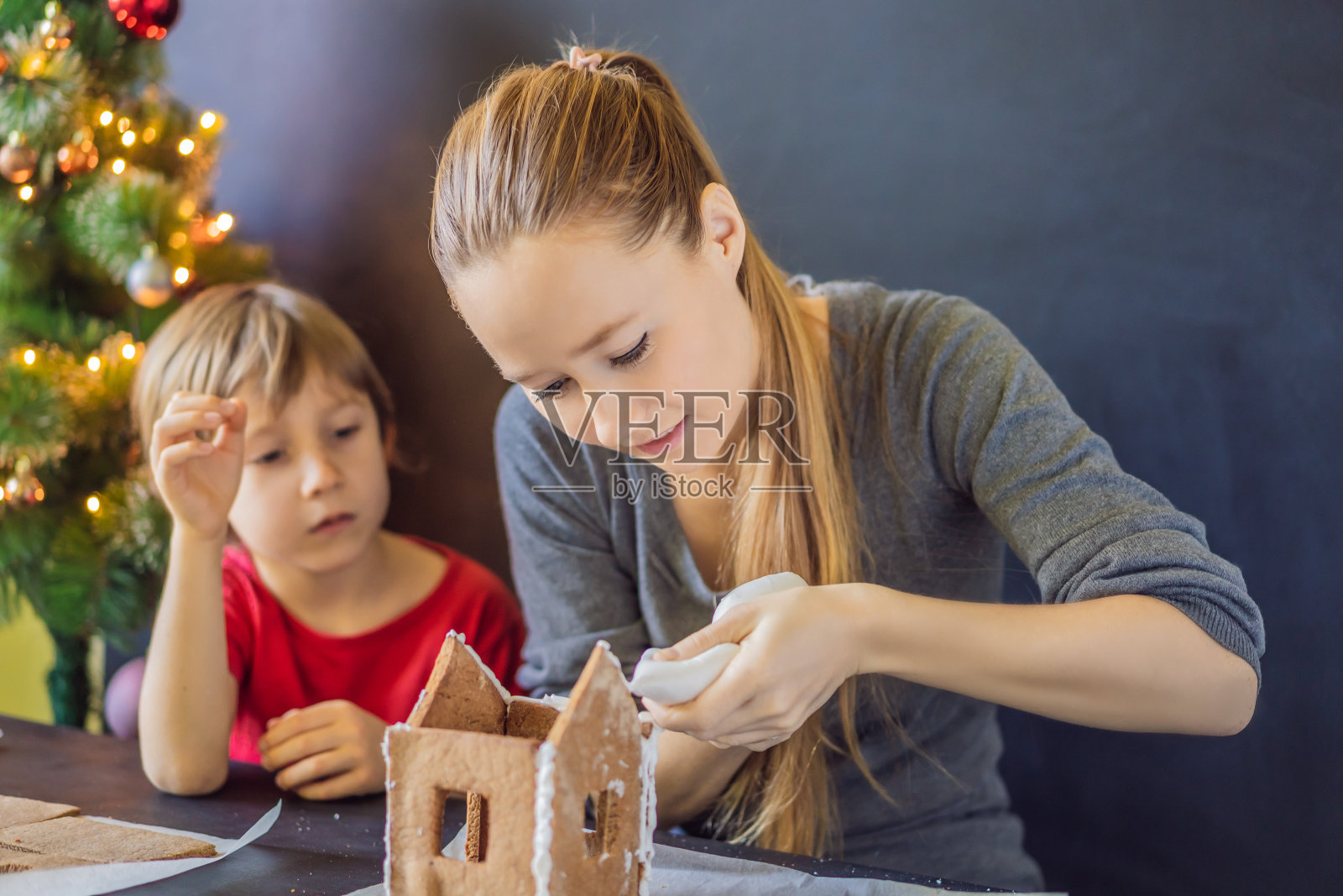 年轻的妈妈和孩子在平安夜做姜饼屋照片摄影图片