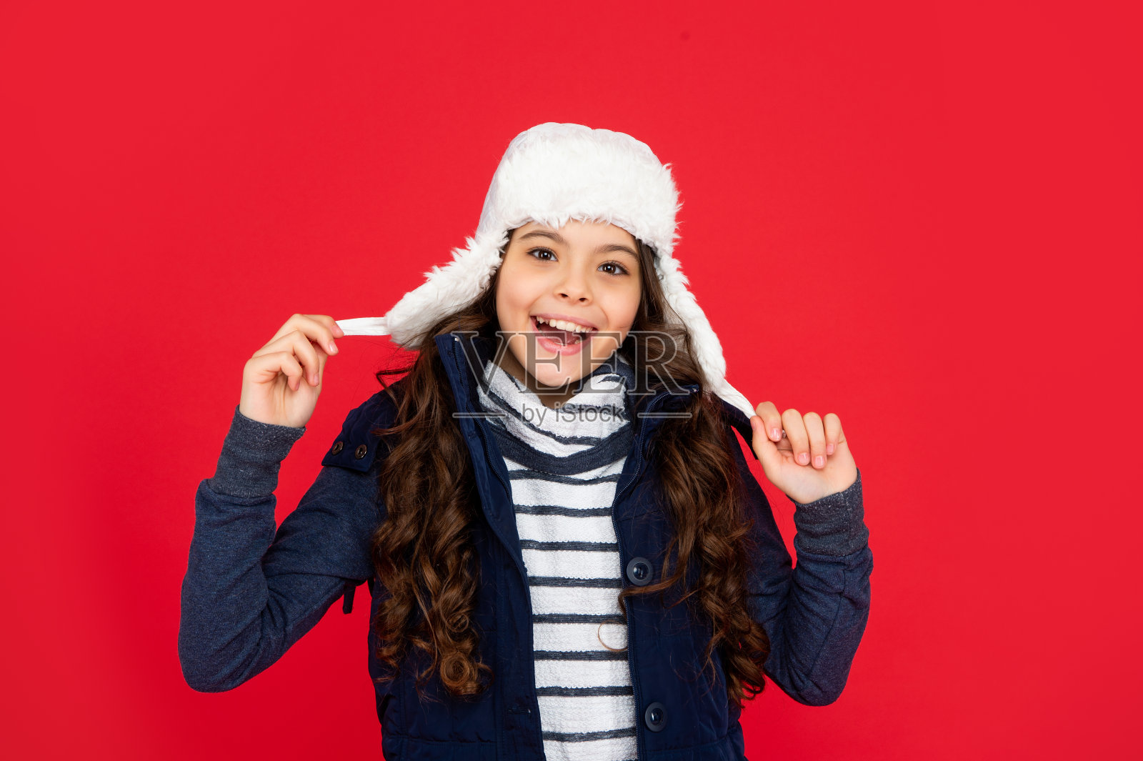 快乐的孩子，卷发，戴着耳塞帽。红色背景的少女。照片摄影图片