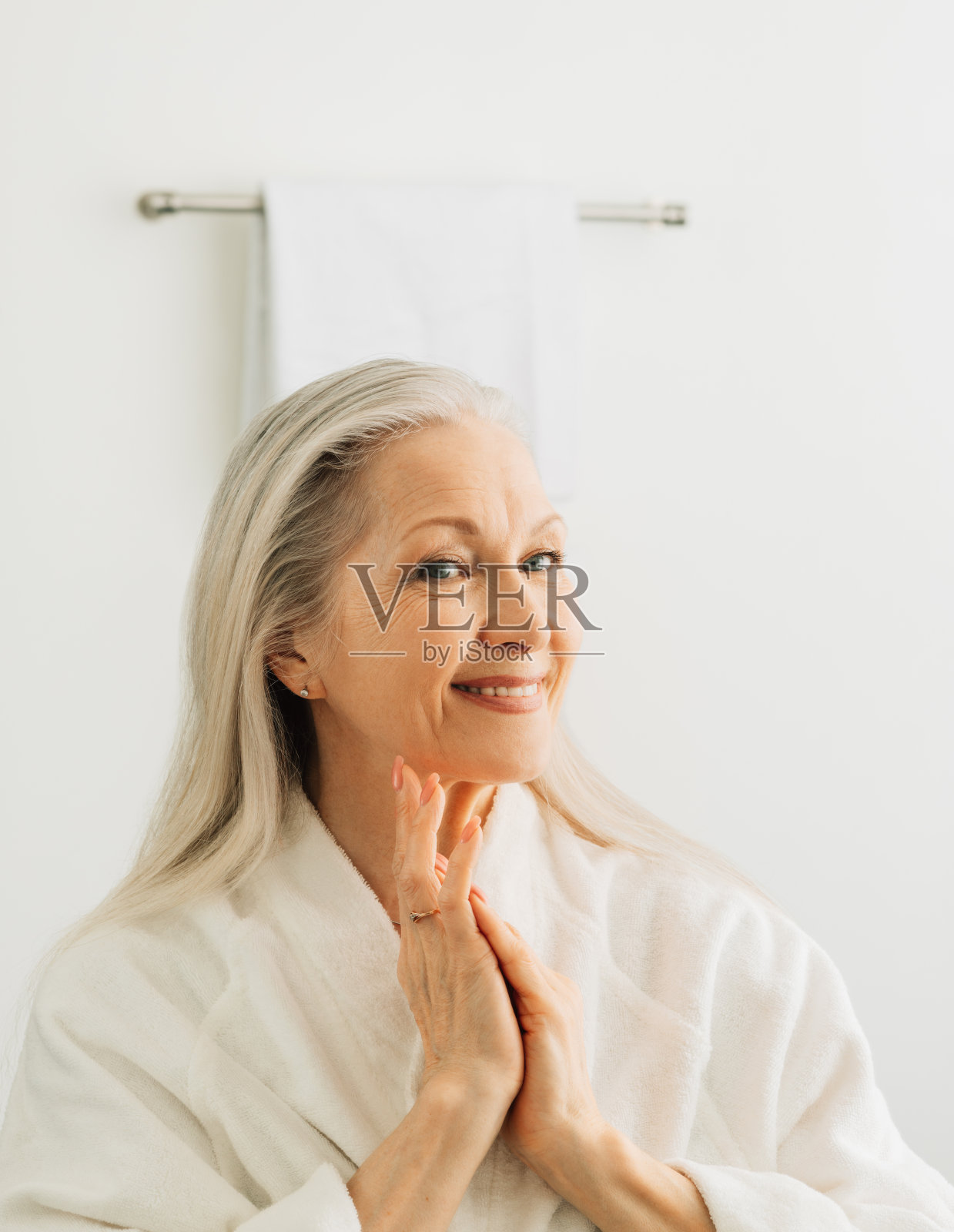 早晨，一位白发苍苍的女性站在浴室的镜子前，微笑着欣赏自己的倒影照片摄影图片