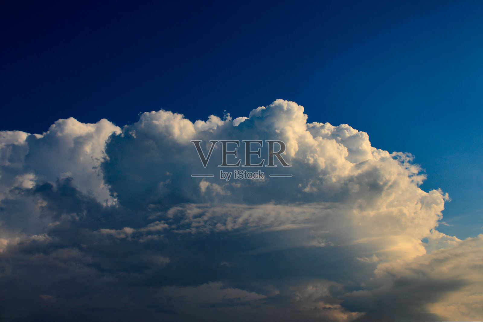 巨大的积云充血云，顶部被照亮，底部有阴影，漂浮在梯度的宝蓝色天空下。照片摄影图片