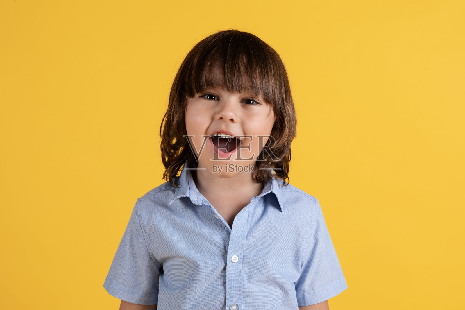 孩子们兴奋。惊讶的小男孩惊奇地用笔嘴看着相机，橙色的画室背景照片摄影图片