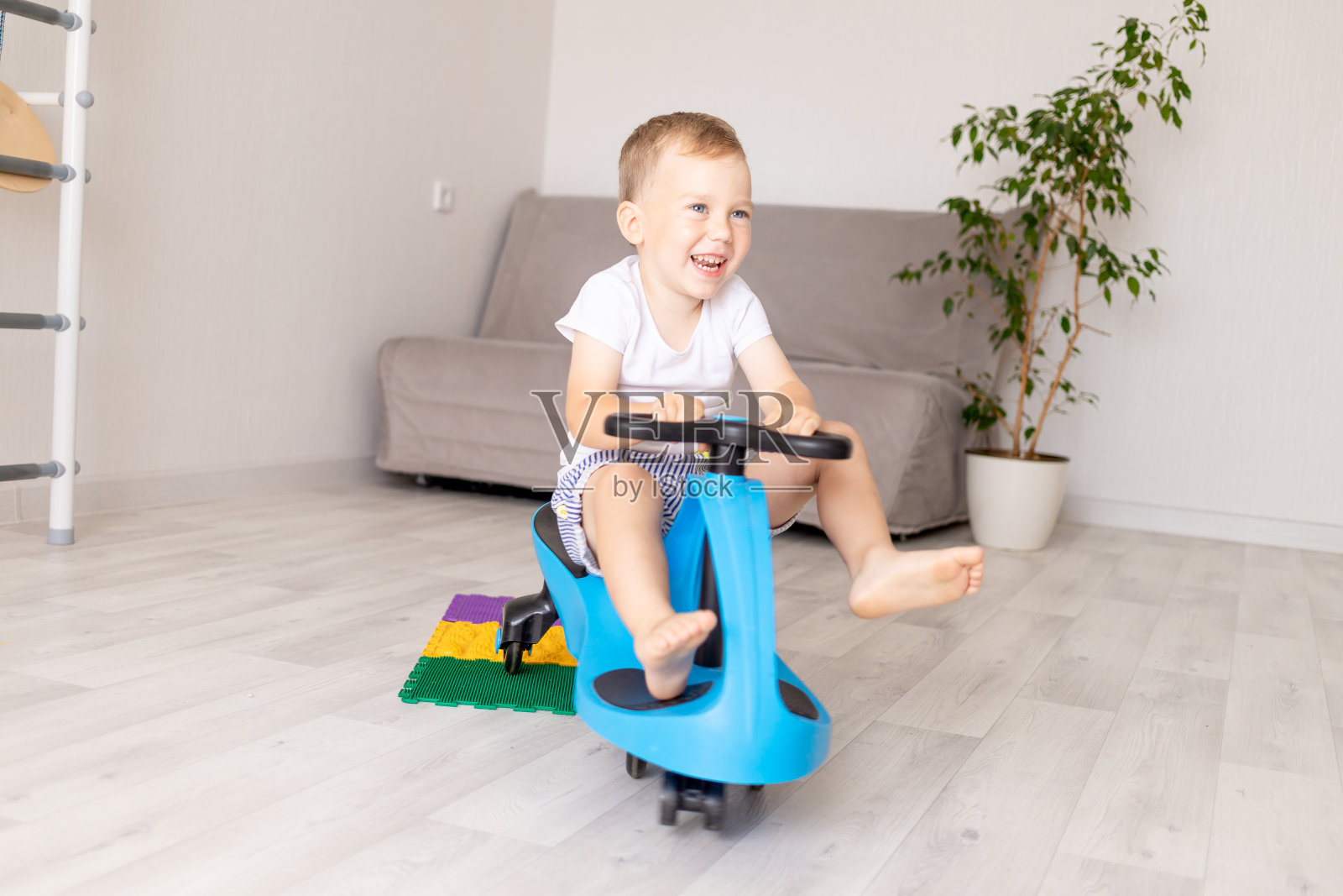 一个快乐的小男孩在家里骑着一辆蓝色的汽车，地板上铺着一块整形地毯照片摄影图片