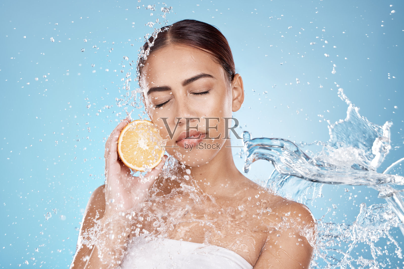 水飞溅，橙色和天然护肤健康在蓝色工作室背景有机面部护理清洁，皮肤排毒和水果营养。模特面部，柑橘维他命c和化妆品清洁照片摄影图片