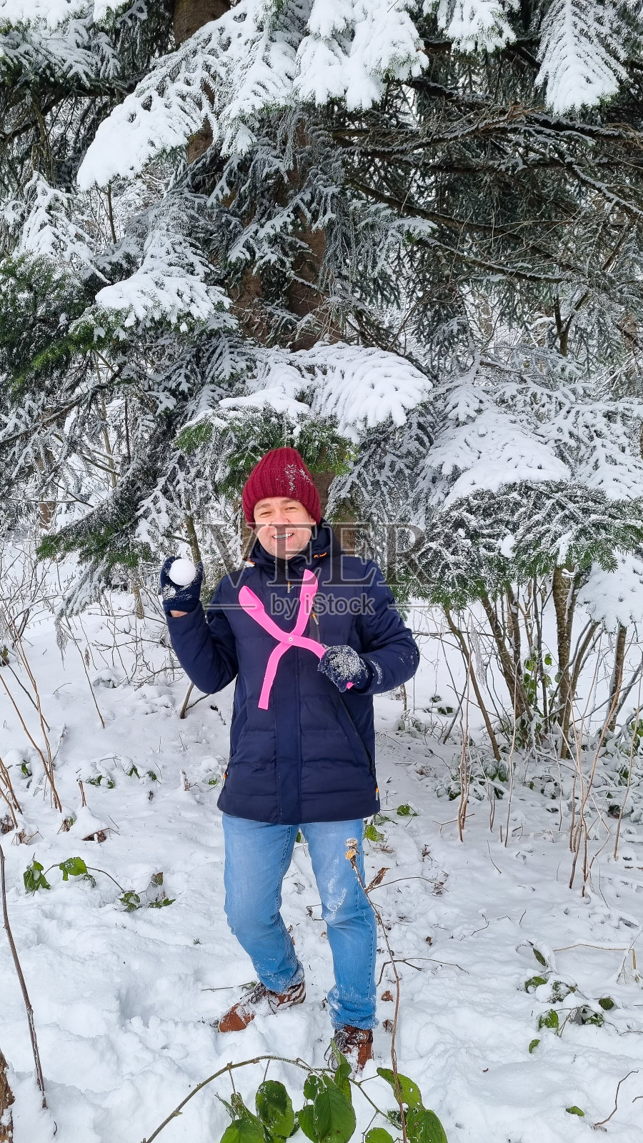雪中云杉树旁，一个兴高采烈的人，手里拿着造雪机和雪球。照片摄影图片