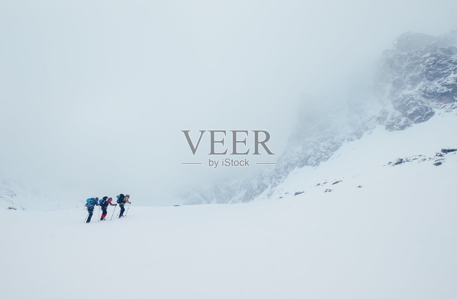 三人绳队攀登高山冬峰。暴风雪覆盖在Lomnicky Stit岩石山下的Vysoke Tatry(高塔特拉斯)山脉的构造盆地。极限运动概念。照片摄影图片