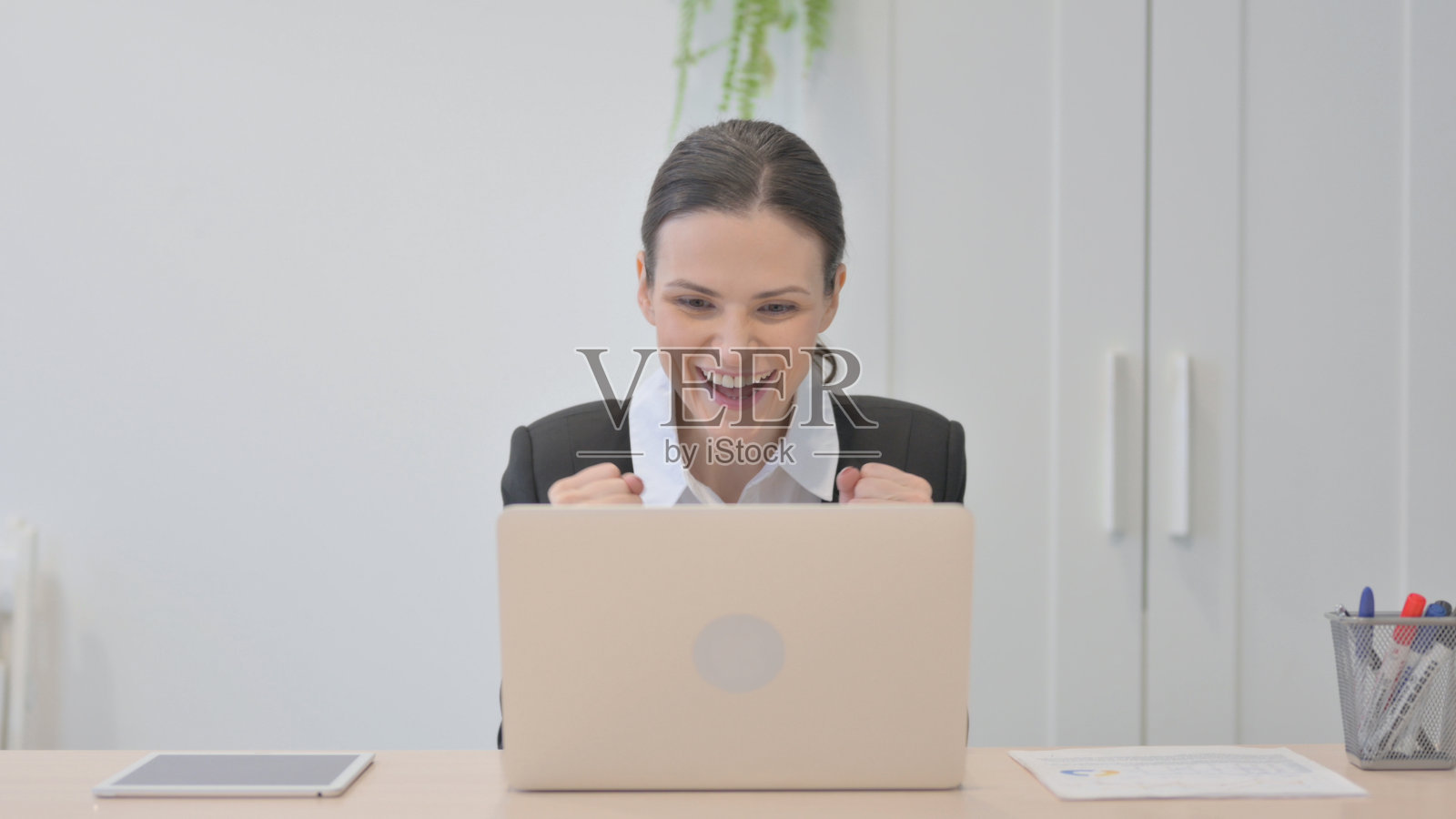 年轻的女商人在办公室的笔记本电脑上庆祝在线成功照片摄影图片