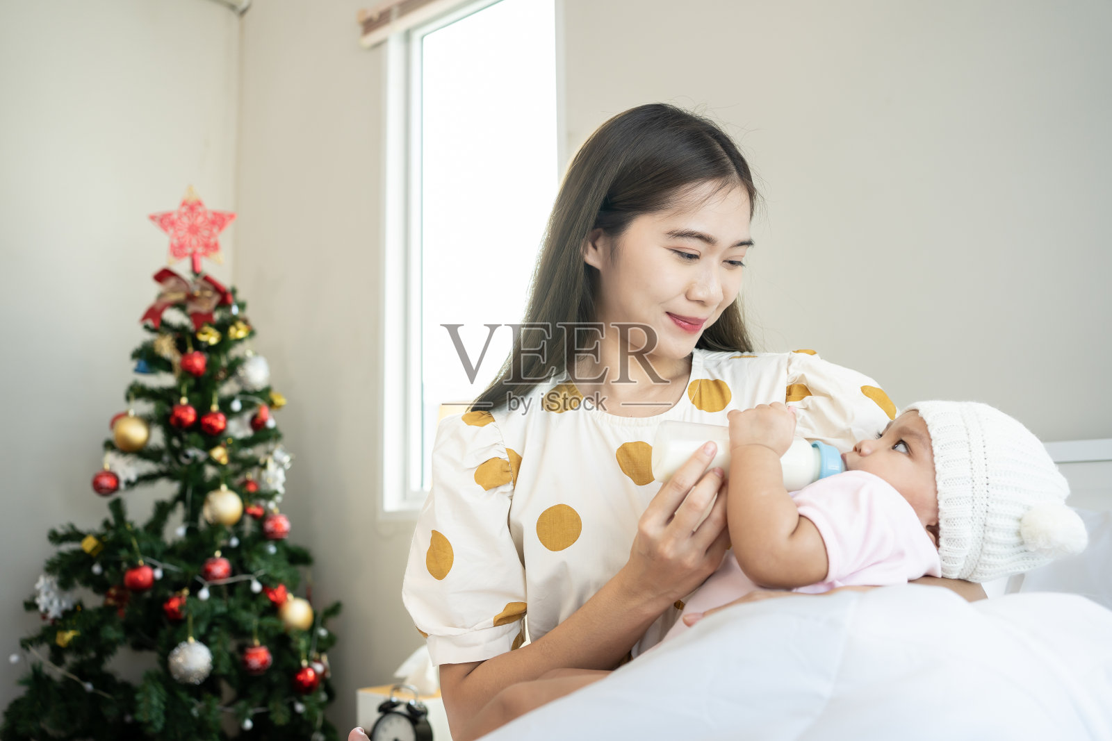 亚洲妈妈在卧室用奶瓶喂宝宝，她感到很幸福。照片摄影图片
