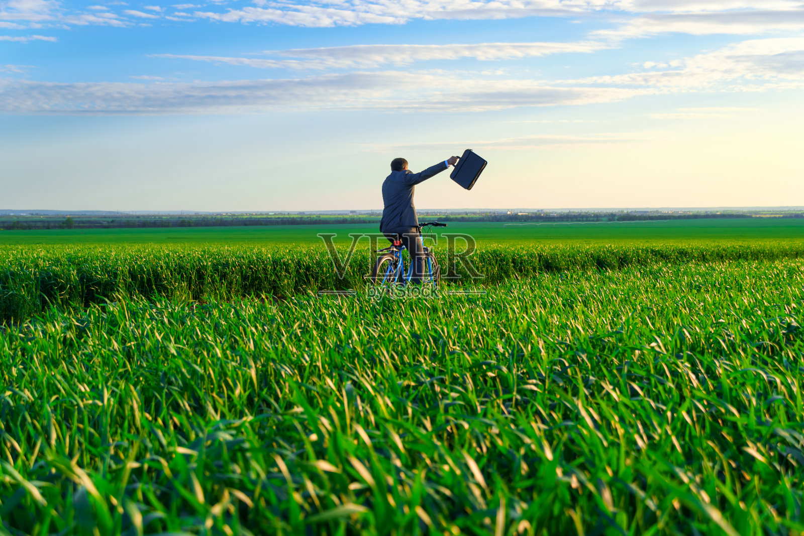 一个商人提着公文包，骑着自行车，站在绿油油的草地上，穿着商务套装，春天美丽的自然，自由职业者的商业理念照片摄影图片