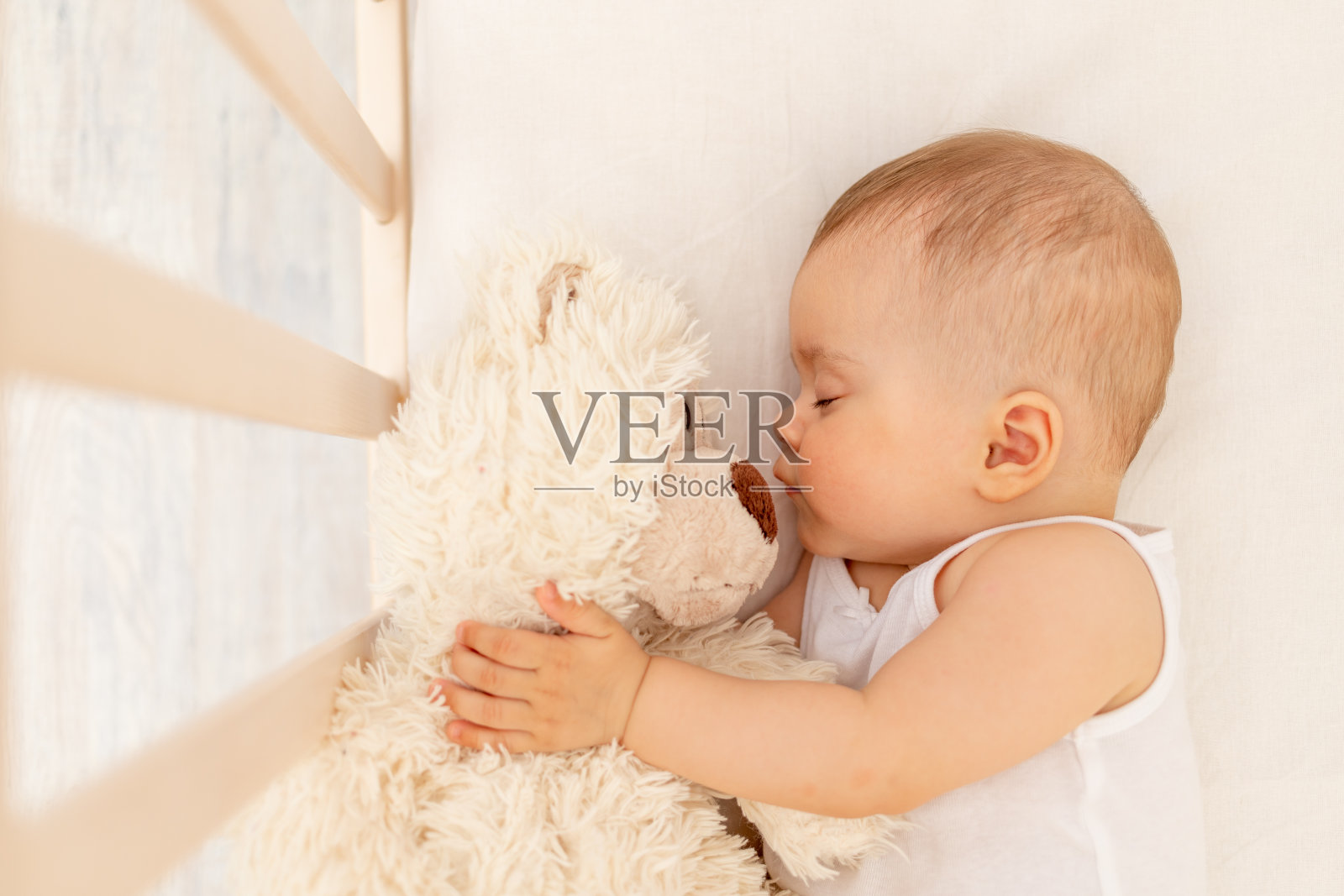 小女婴睡在白色的床上，有一只柔软的小熊，健康的婴儿睡眠照片摄影图片