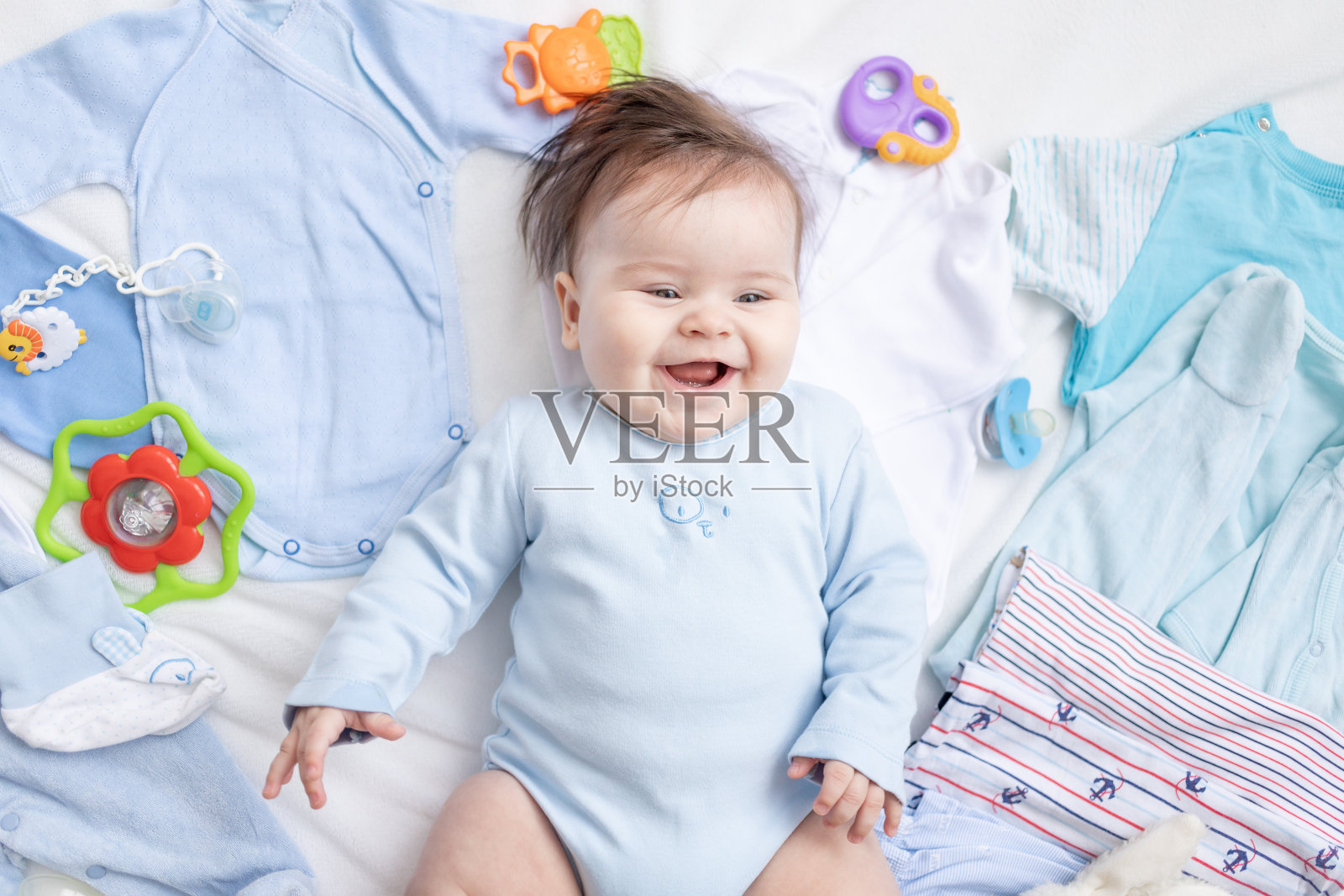 一个穿着蓝色衣服的婴儿躺在儿童饰品和衣服中间照片摄影图片
