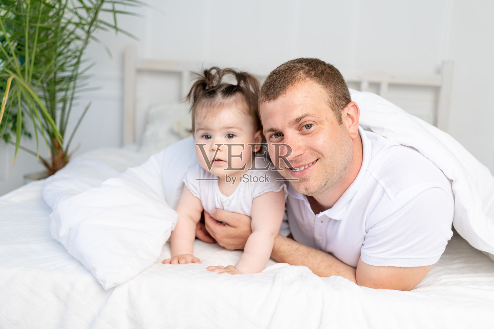 爸爸和小女儿在床上盖着毯子，微笑着拥抱着。全家快乐，父亲节快乐照片摄影图片