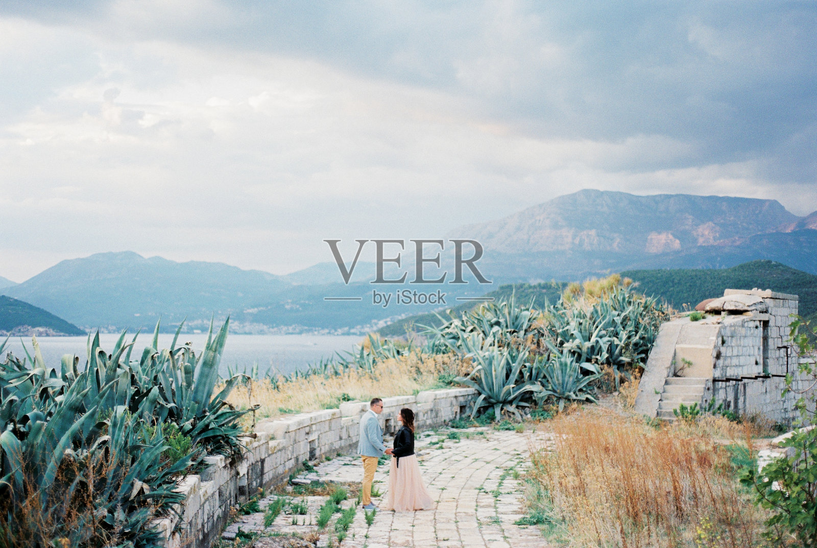 新娘和新郎站在龙舌兰丛附近一个圆形石台的废墟上照片摄影图片