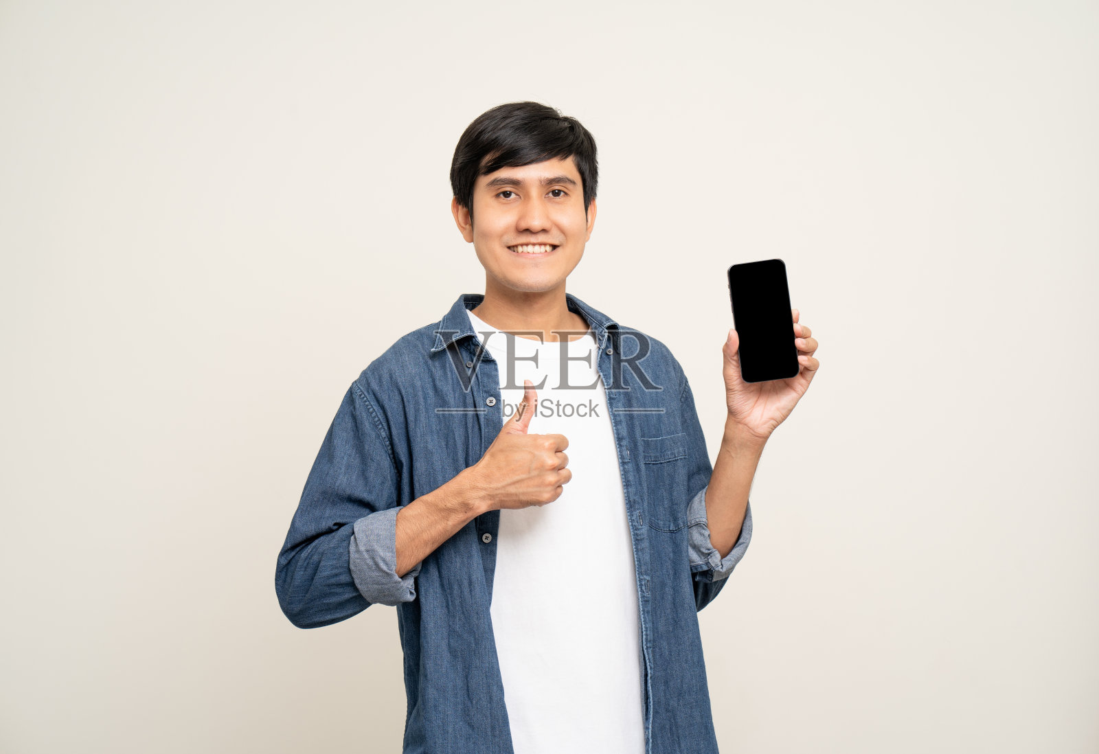 年轻的亚洲男子站在孤立的白色背景上使用智能手机。他在用手机发短信。搭配夹克和牛仔裤。年龄25岁左右。照片摄影图片